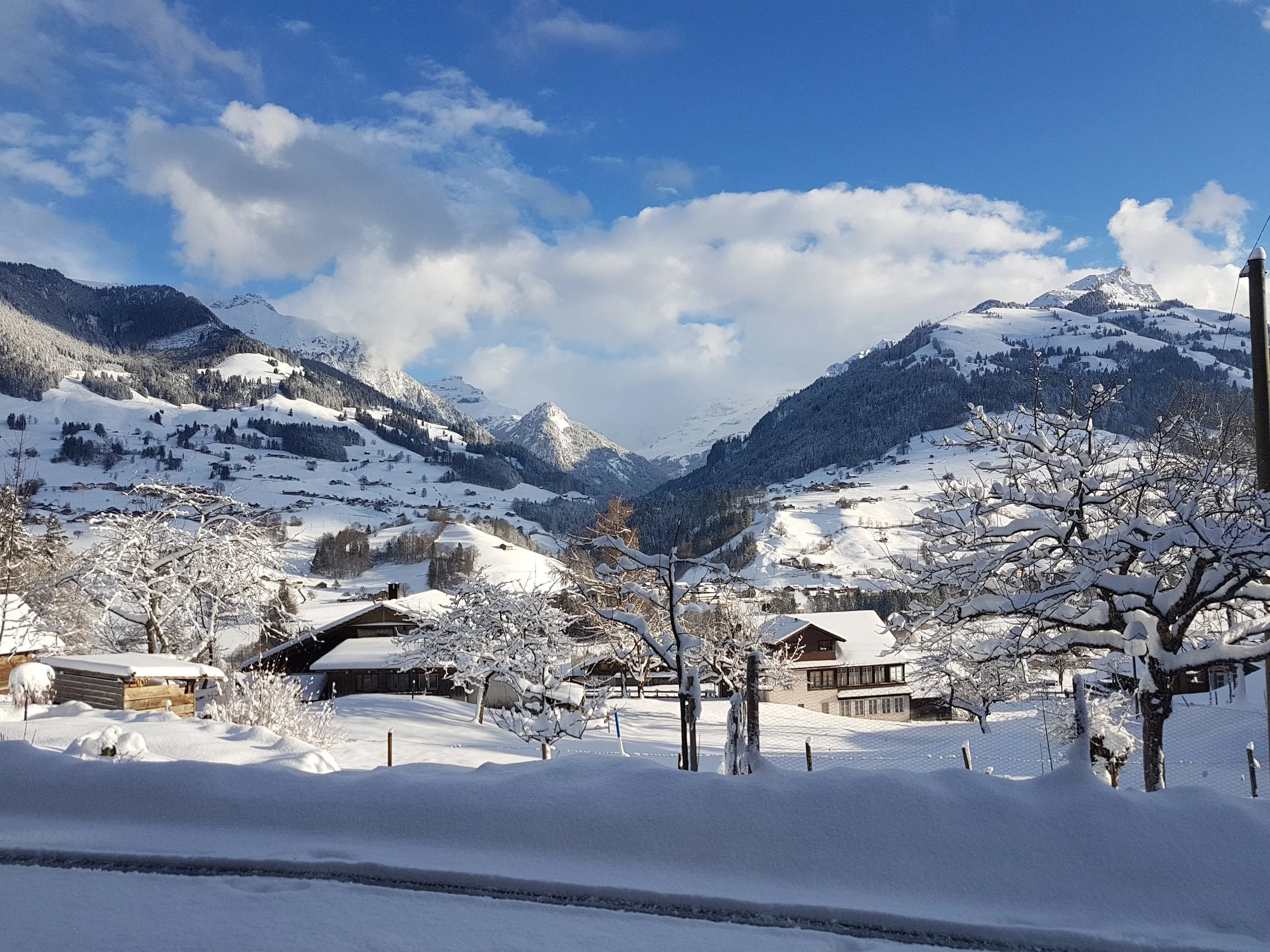 Verschneite Berge und Hütten in einer winterlichen Landschaft, unter einem blauen Himmel mit Wolken