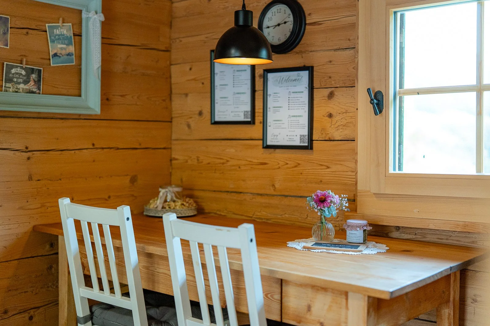 Innenraum eines Holzrestaurants mit einem Tisch, weißen Stühlen, einer Vase mit Blumen, Fenster, Wanddekorationen, einer Uhr und einer Menükarte.