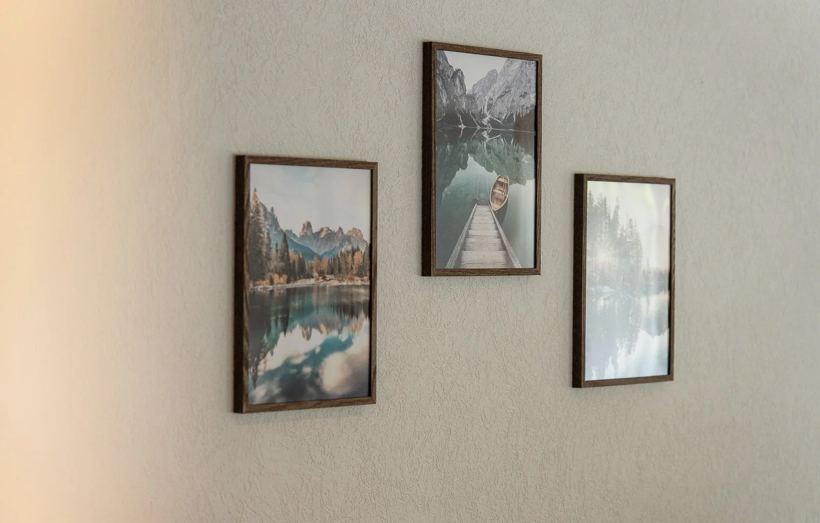Drei Bilderrahmen mit Naturfotografien an einer hellen Wand, zeigen Bergseen und Berge in der Natur.