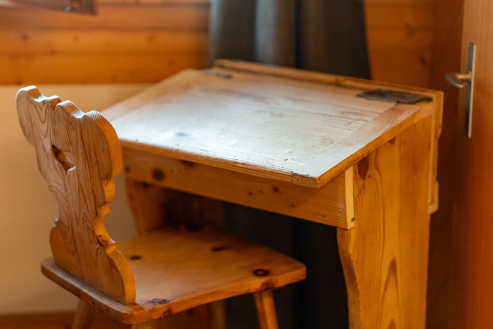 Ein aus Holz gefertigter Schreibtisch mit passendem Stuhl, beide aus naturbelassenem Holz, stehen in einem Raum mit Holzverkleidung an der Wand.