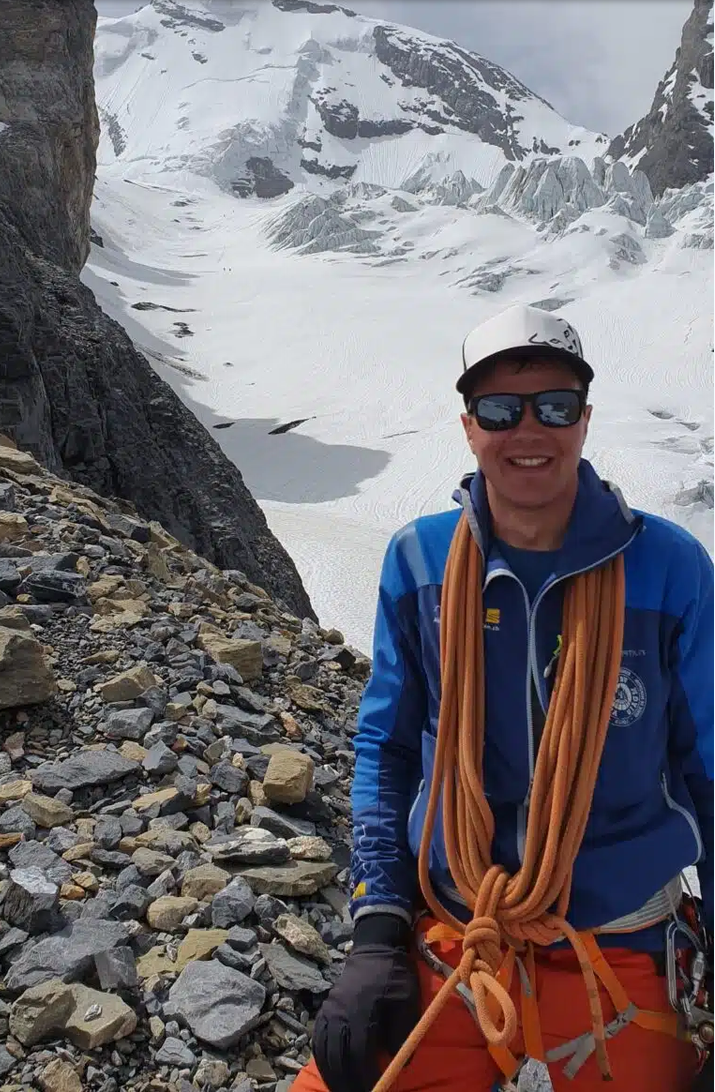Ein Mann in Kletterausrüstung vor einer schneebedeckten Berglandschaft und Gletschern.