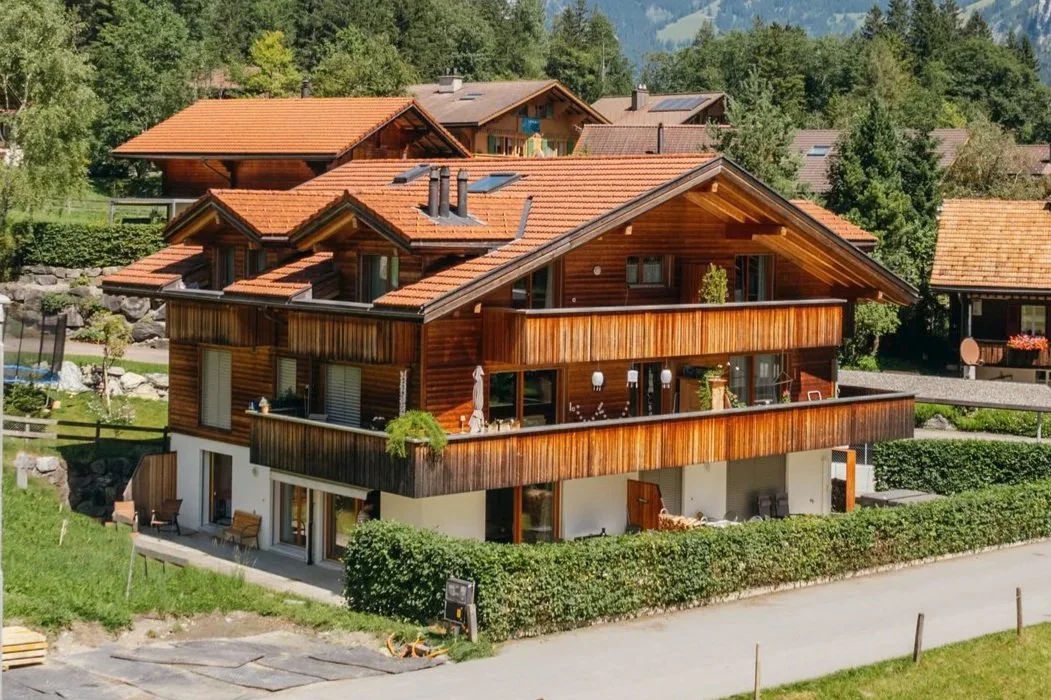 Mehrstöckiges Chalet mit Holzfassade und terrassen, umgeben von grünen Gärten und Bäumen, in einer ländlichen Gegend.