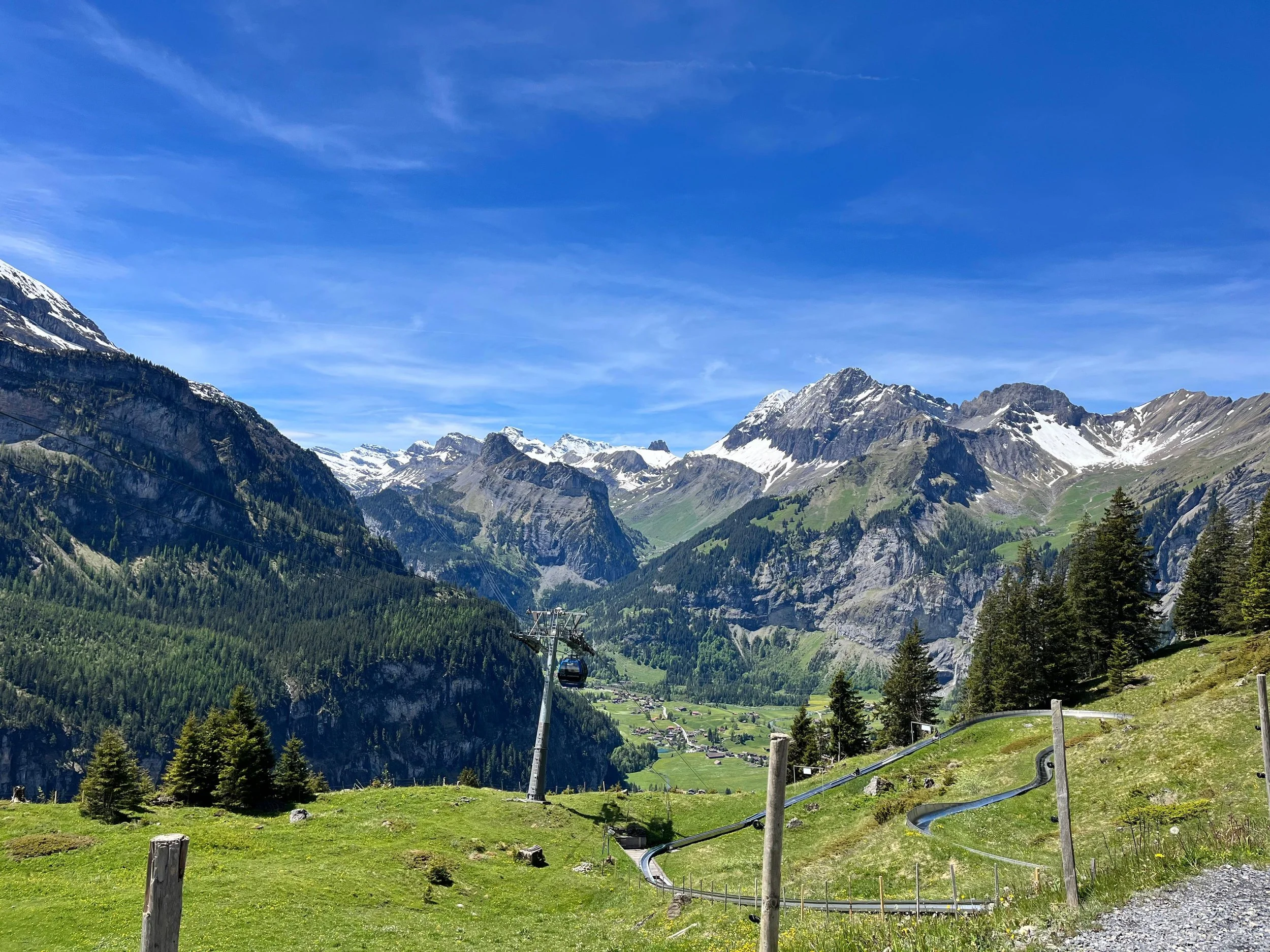 Berglandschaft in den Alpen mit schneebedeckten Gipfeln, grünen Wäldern und einer Seilbahn im Vordergrund