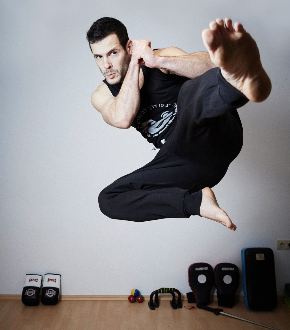 Man performing a martial arts kick in a room with martial arts equipment on the floor.