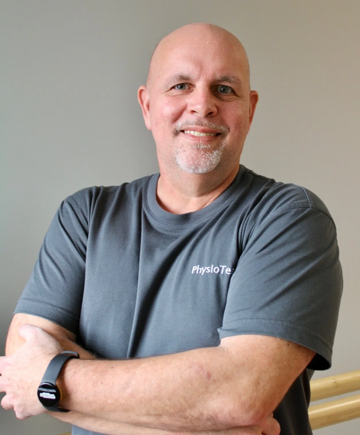 Ein Mann mit kurzhaarigem, grauem Bart trägt ein dunkles T-Shirt und posiert vor einer neutralen Wand.