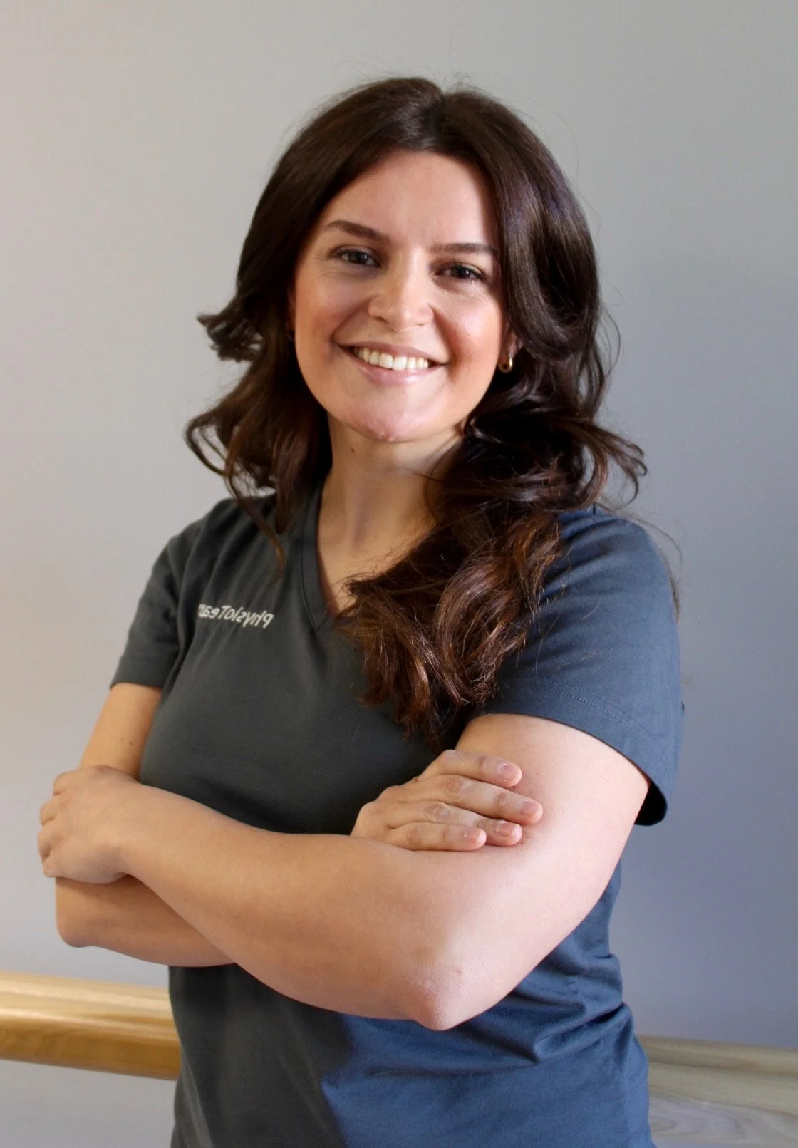Frau mit braunen Haaren, lächelnd, trägt ein dunkles T-Shirt, steht vor einer neutralen Wand.