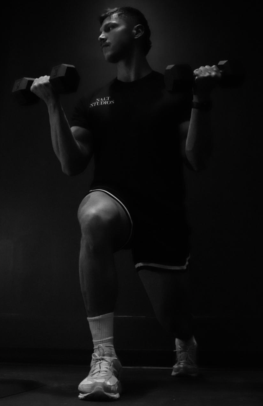 A man lifting dumbbells in a dark room, performing a knee lift exercise.