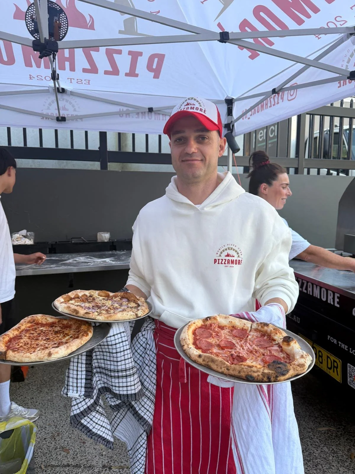 Michele holding freshly cooked pizzas under the Pizzamorè catering gazebo.