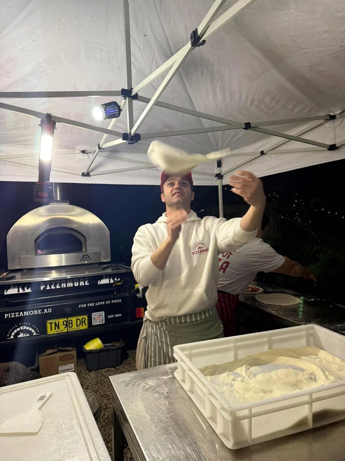 Michele tossing pizza dough beside the Pizzamorè mobile wood-fired oven.