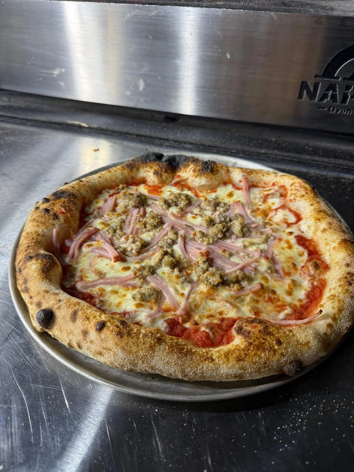 Freshly baked pizza with cheese, ham, and sausage on a metal tray.