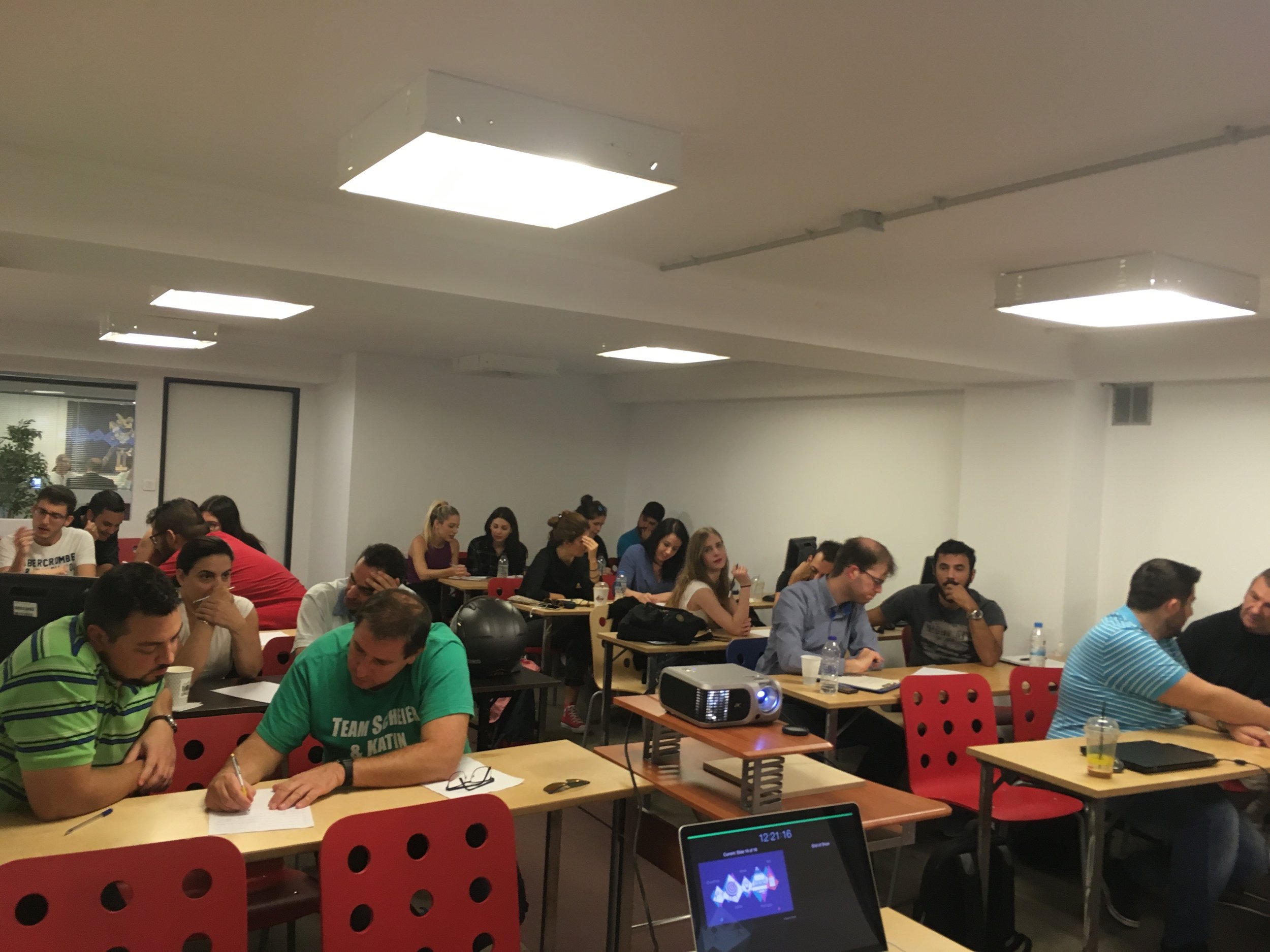 People seated at tables in a classroom or conference room, engaged in discussions.