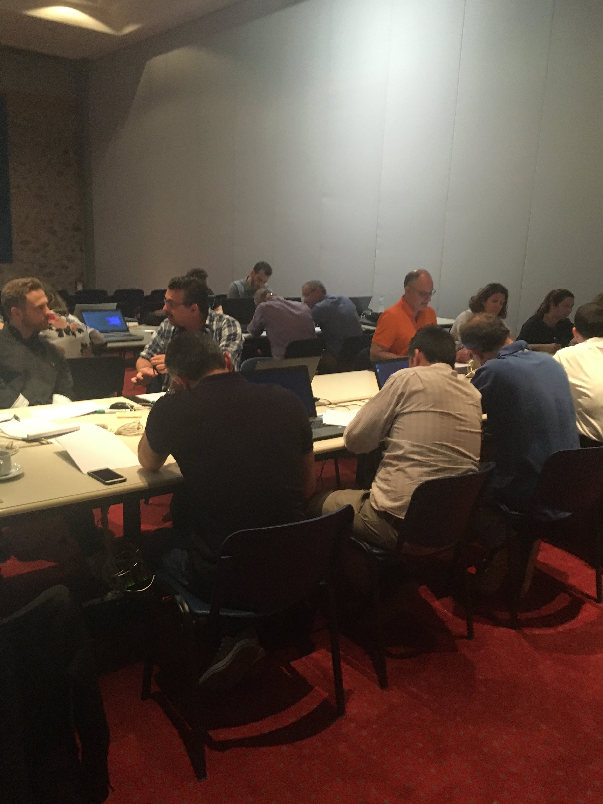 Group of people working on laptops and having discussions at a conference table in a meeting room.