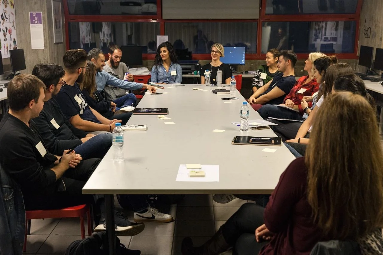 Group of people sitting around a conference table in a meeting room, engaging in a discussion or presentation.