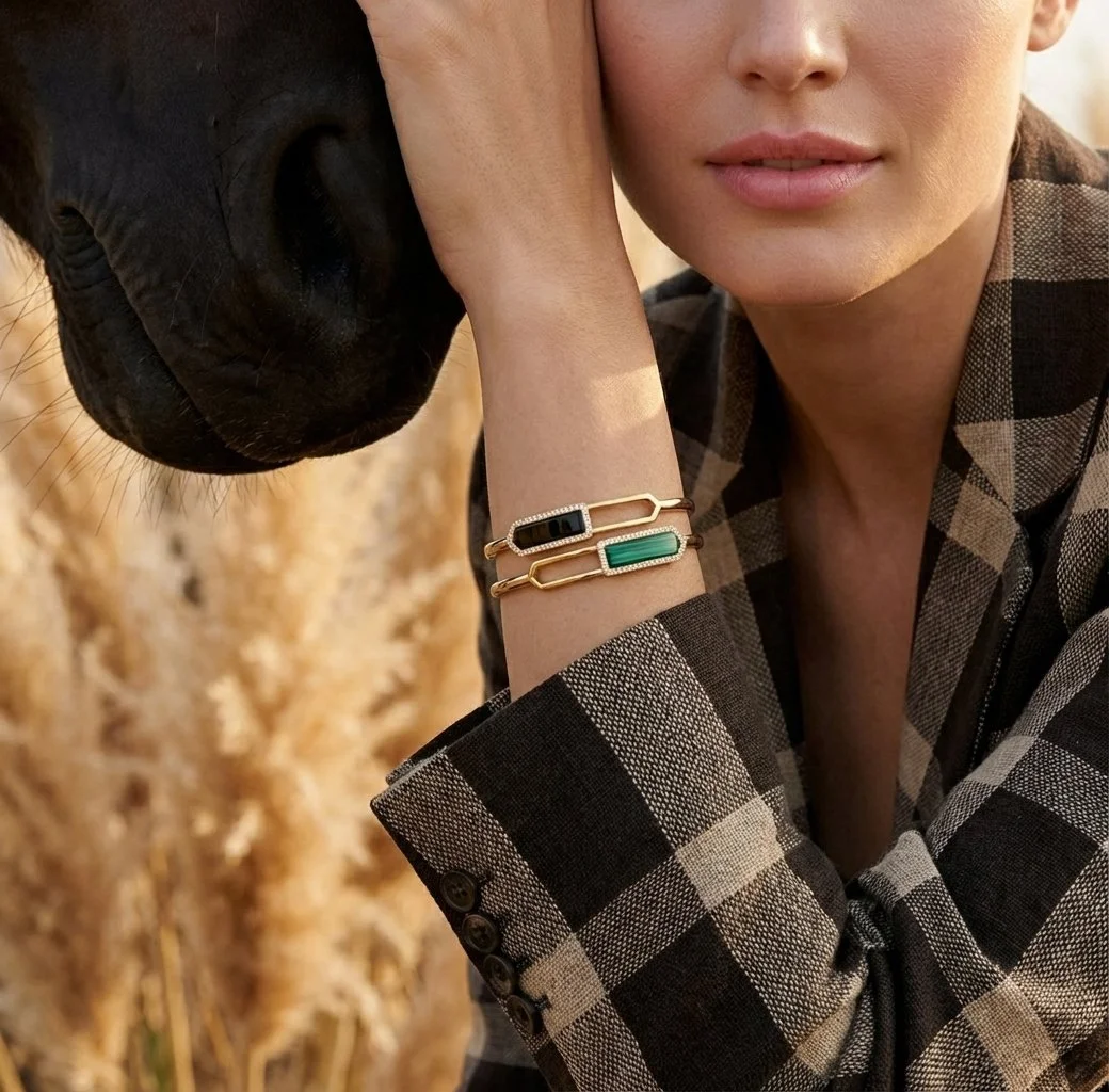 Close-up of a woman in a black and beige plaid blazer leaning her face while touching a horse's snout, wearing a dual stone in onyx and malachite in rectangular shape on one end and pointed edges facing out in sterling silver and yellow gold vermeil.