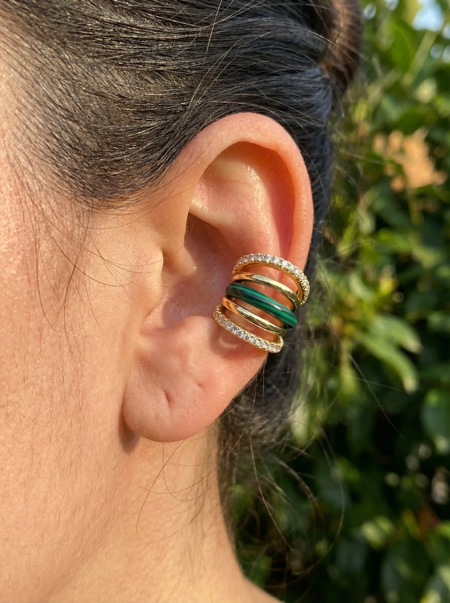 Close-up of a person's ear wearing a 5-band ear cuff in sterling silver with gold vermeil, malachite, and diamond-encrusted bands, and dark hair in the background.