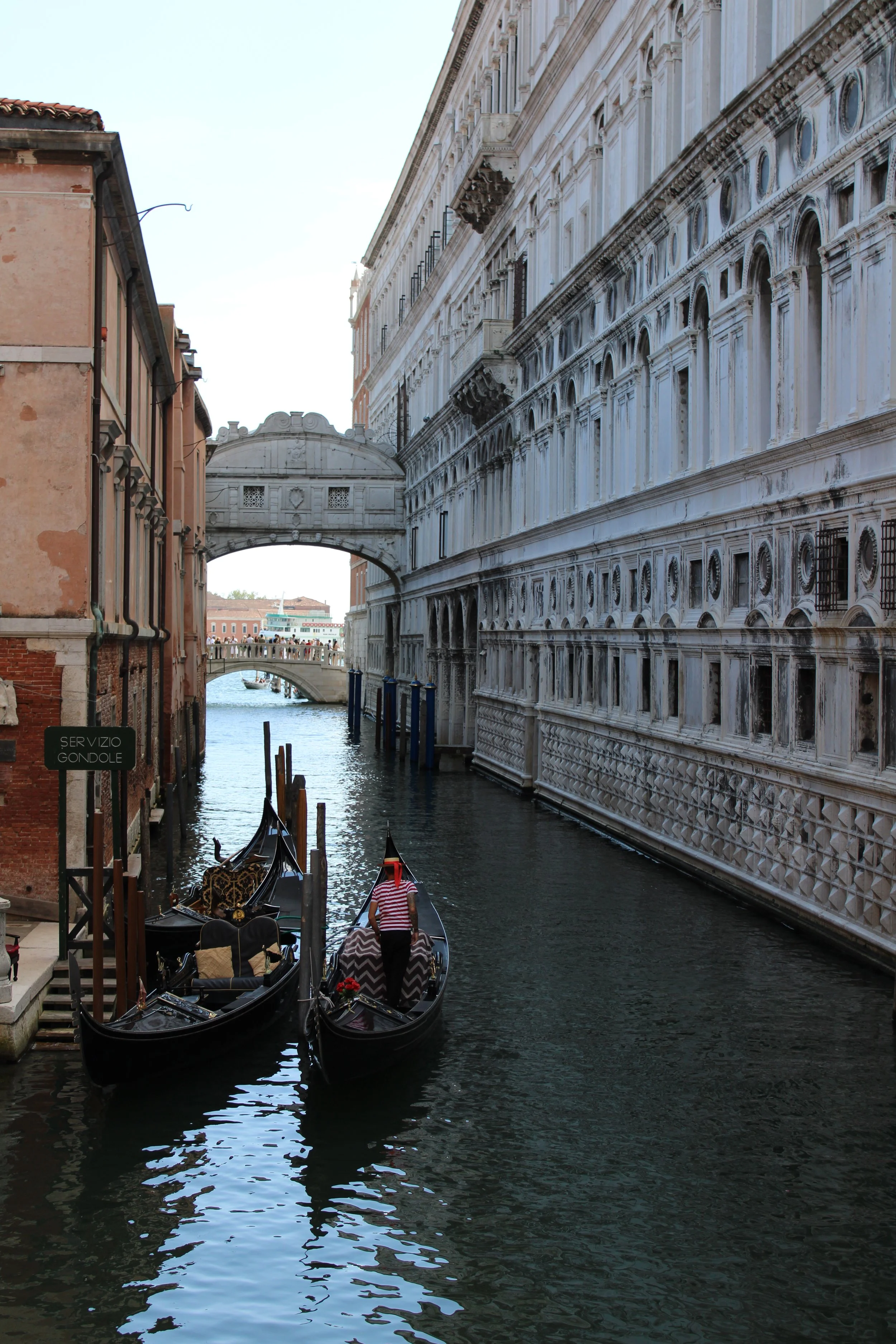 Gondola on a canal in Venice, Italy, with historic buildings and a stone bridge in the background.