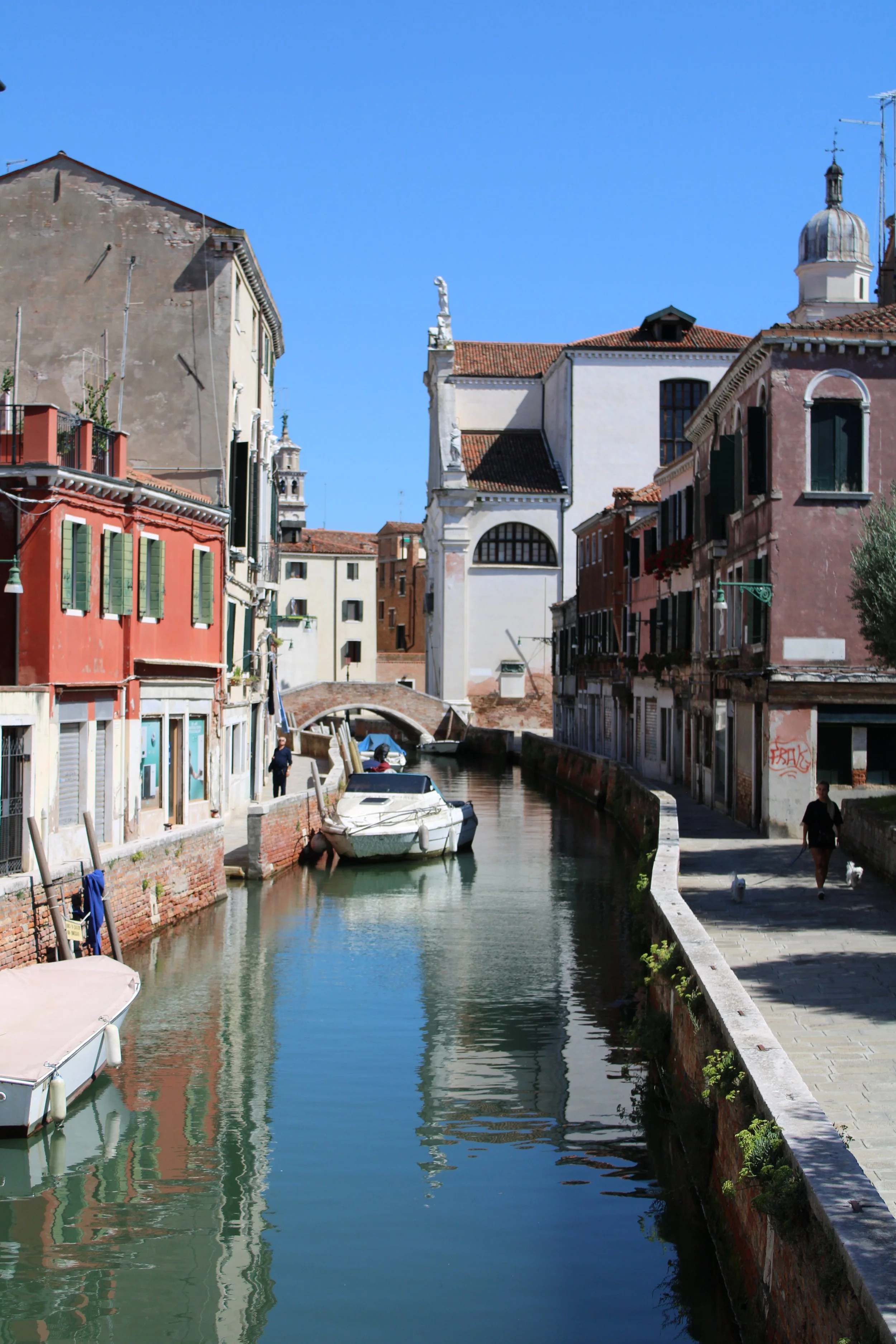 A canal scene in Venice with boats, colorful buildings, and clear blue sky.
