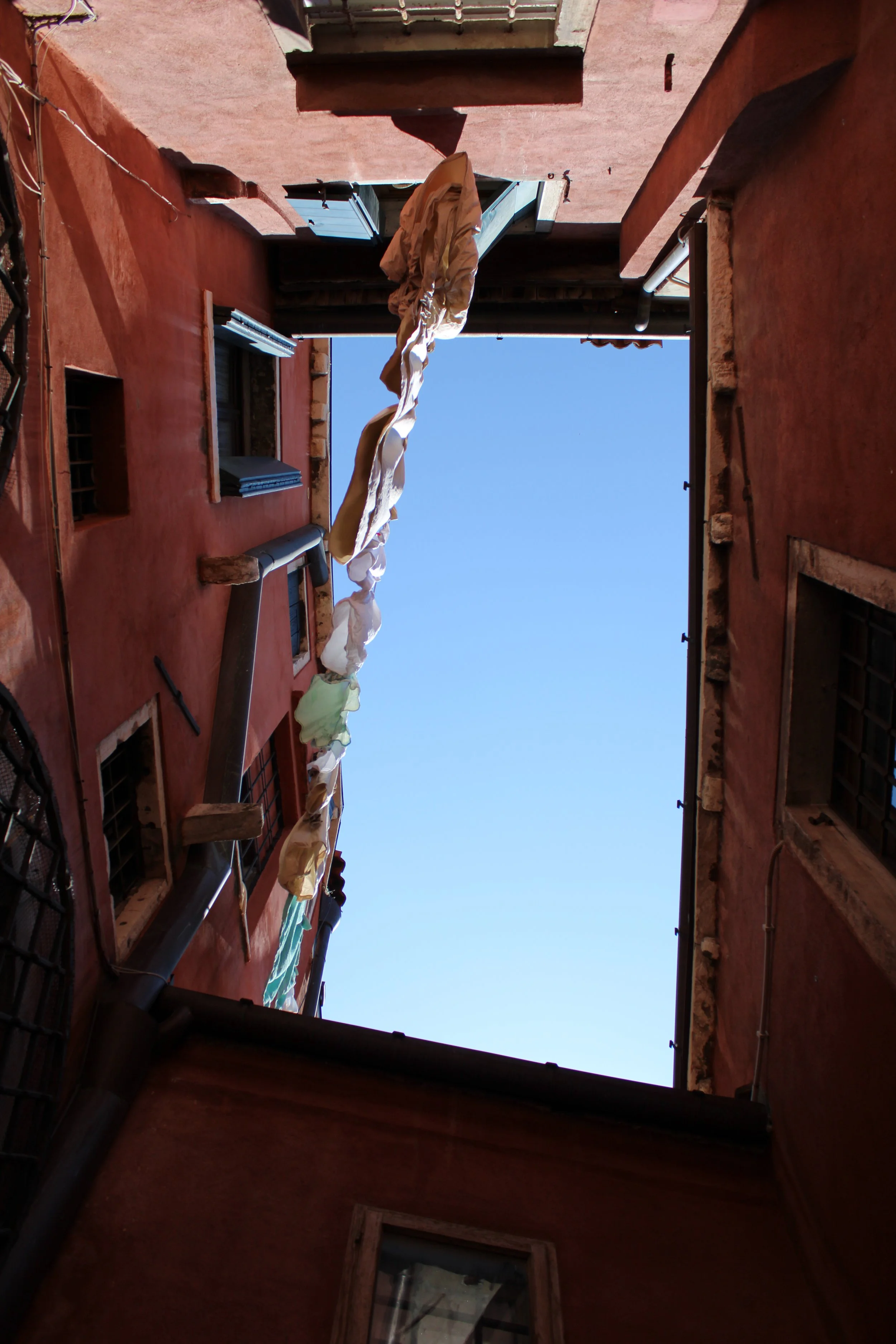 View looking up at the sky through a courtyard of red buildings with laundry hanging across.