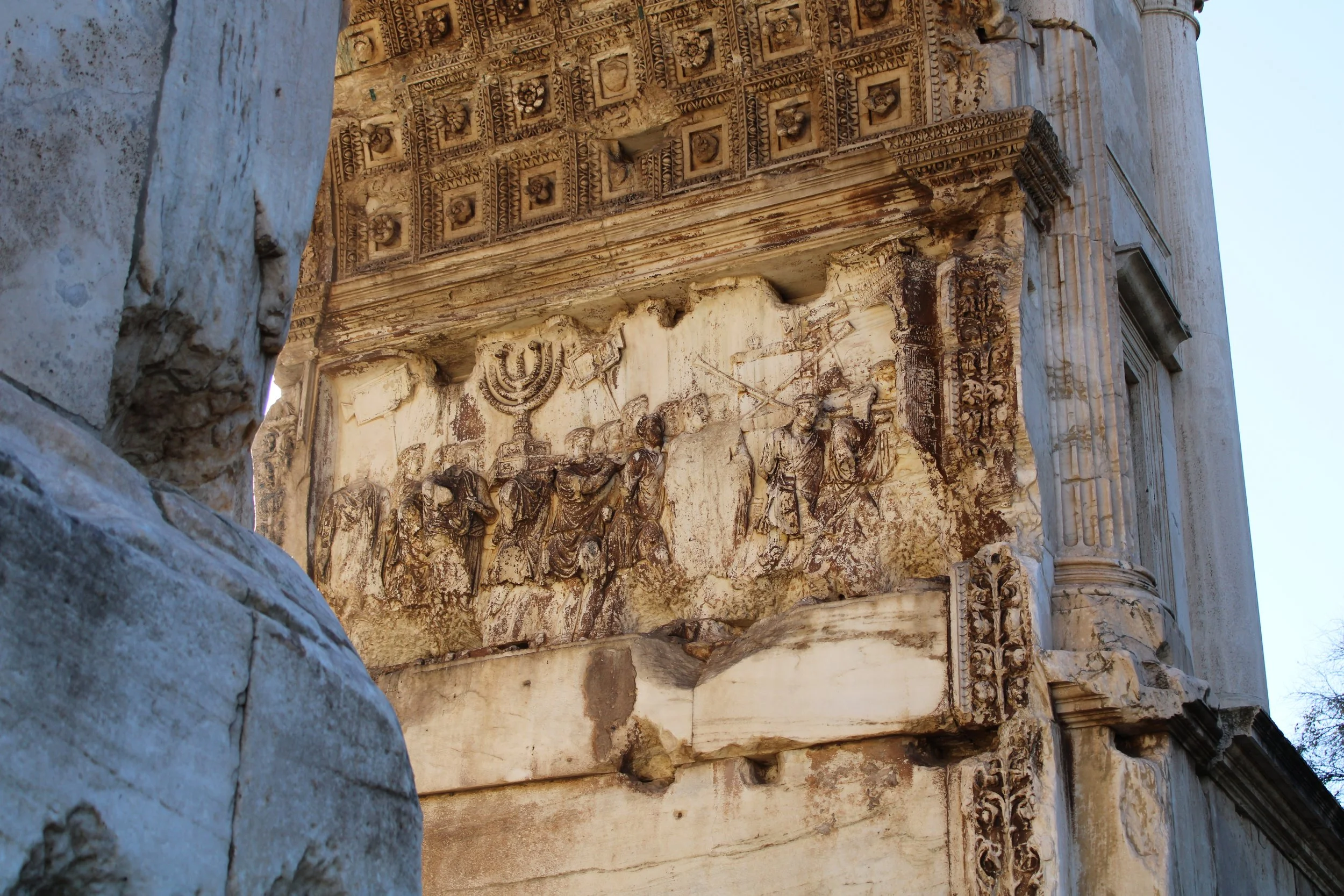 Ancient stone relief carving on a historical building showing figures, a menorah, and other decorative designs.