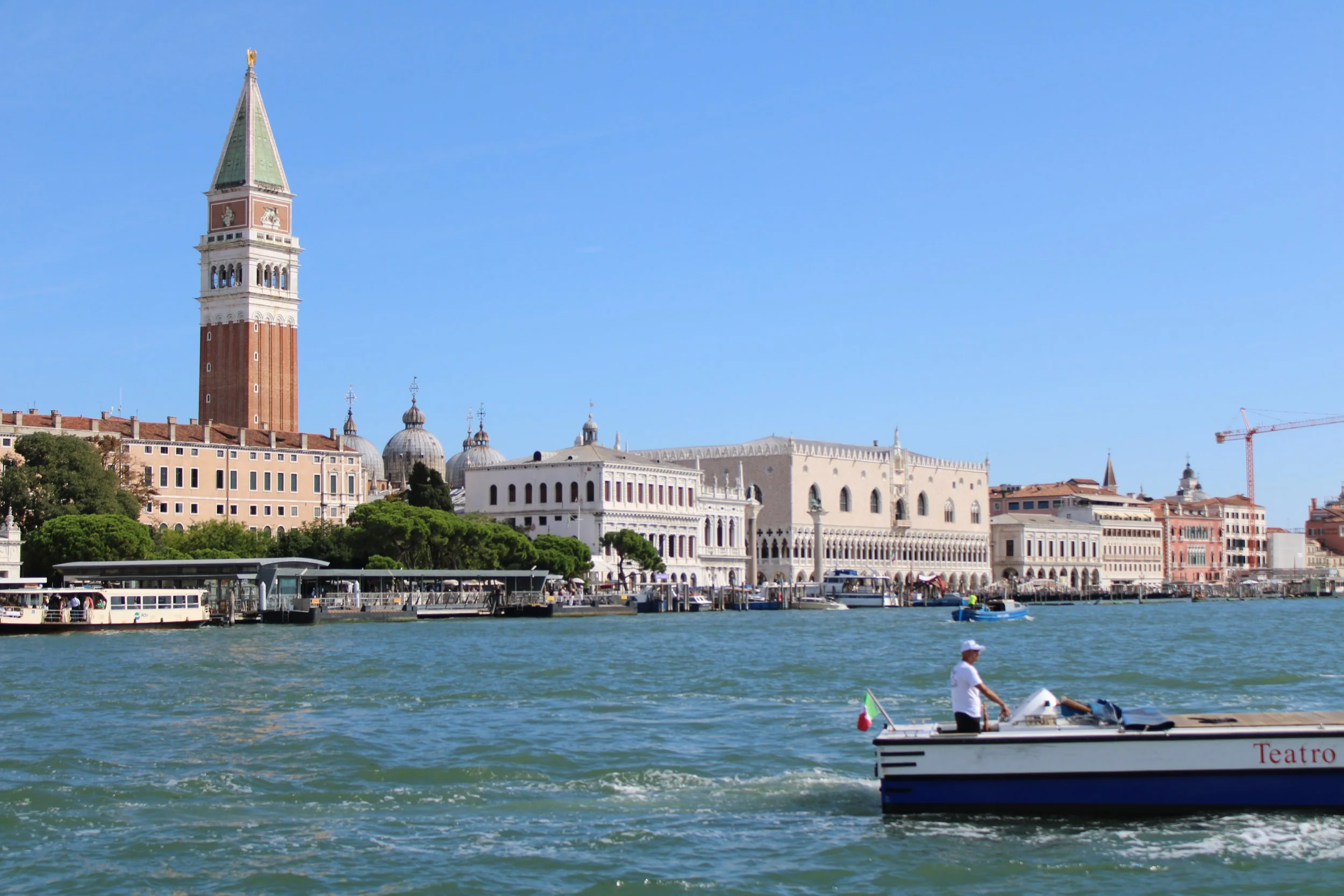Picturesque view of Venice, Italy, featuring the iconic St. Mark's Campanile, historic buildings along the water's edge, and a boat with a person on it in the foreground.