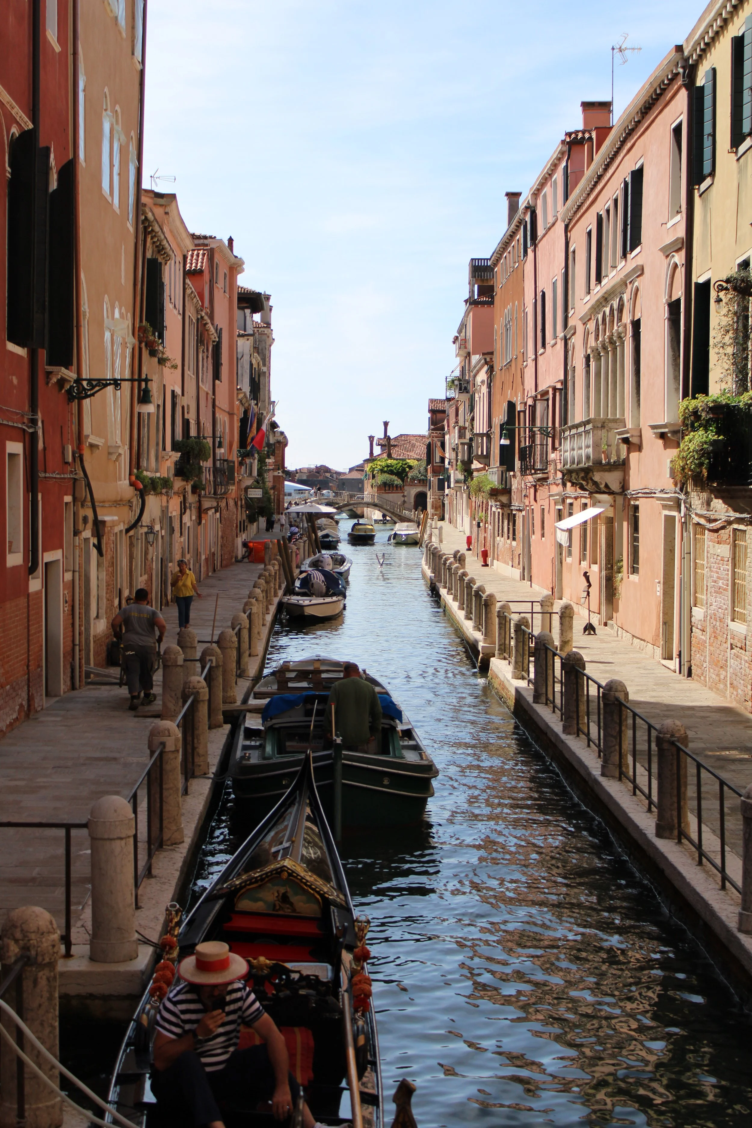 A canal in Venice, Italy, with boats docked, colorful buildings on either side, and a small bridge in the distance.