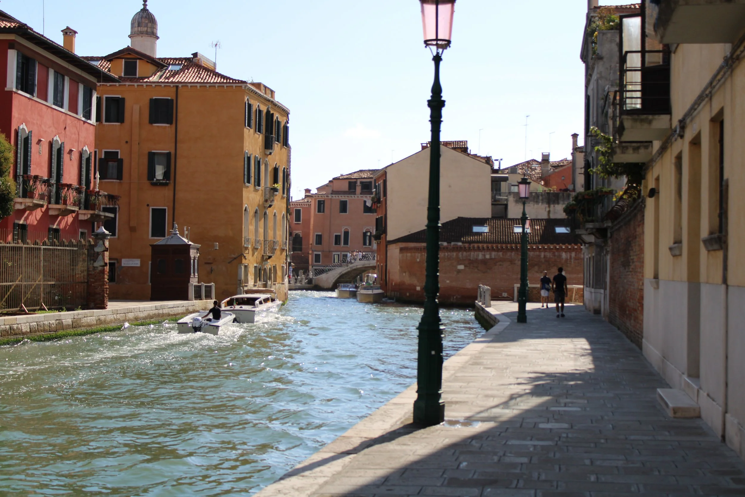 Colorful buildings along a canal with boats and a paved walkway,Venice, Italy.
