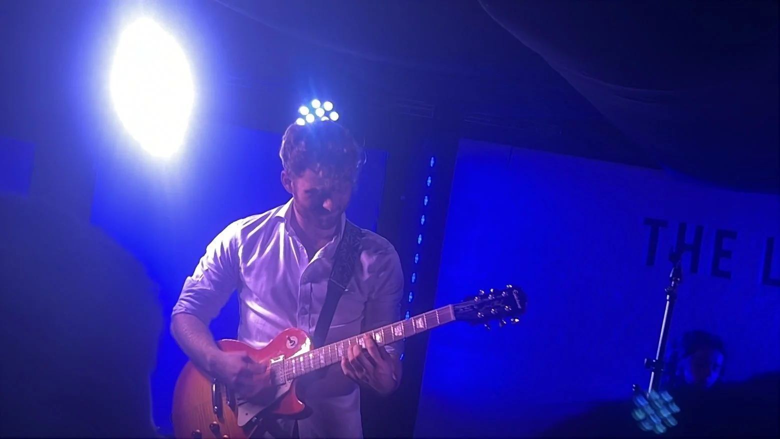 A person playing an electric guitar on stage under blue and purple lighting.