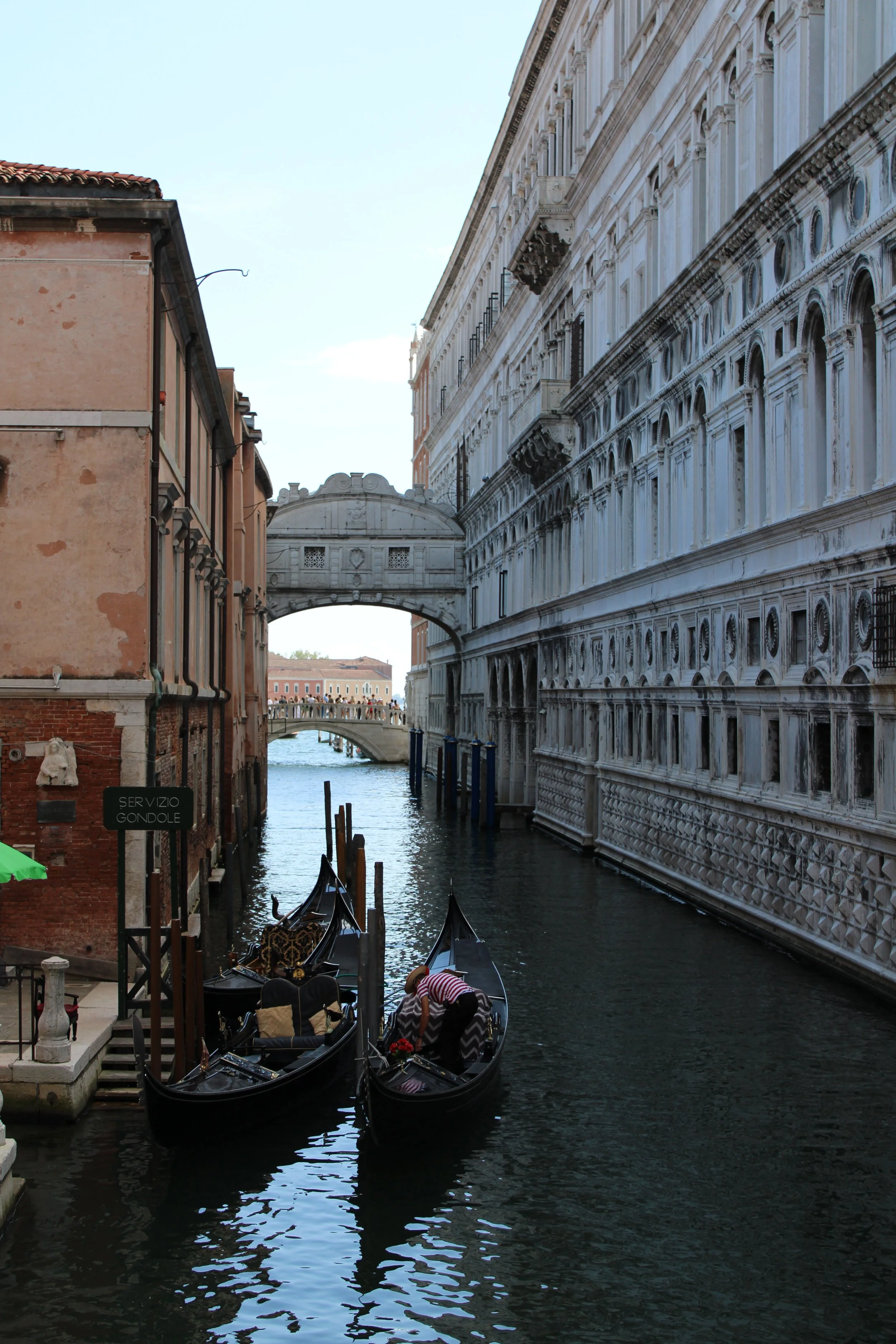 Gondolas in a canal in Venice, Italy, with historic buildings on either side and a bridge in the background.