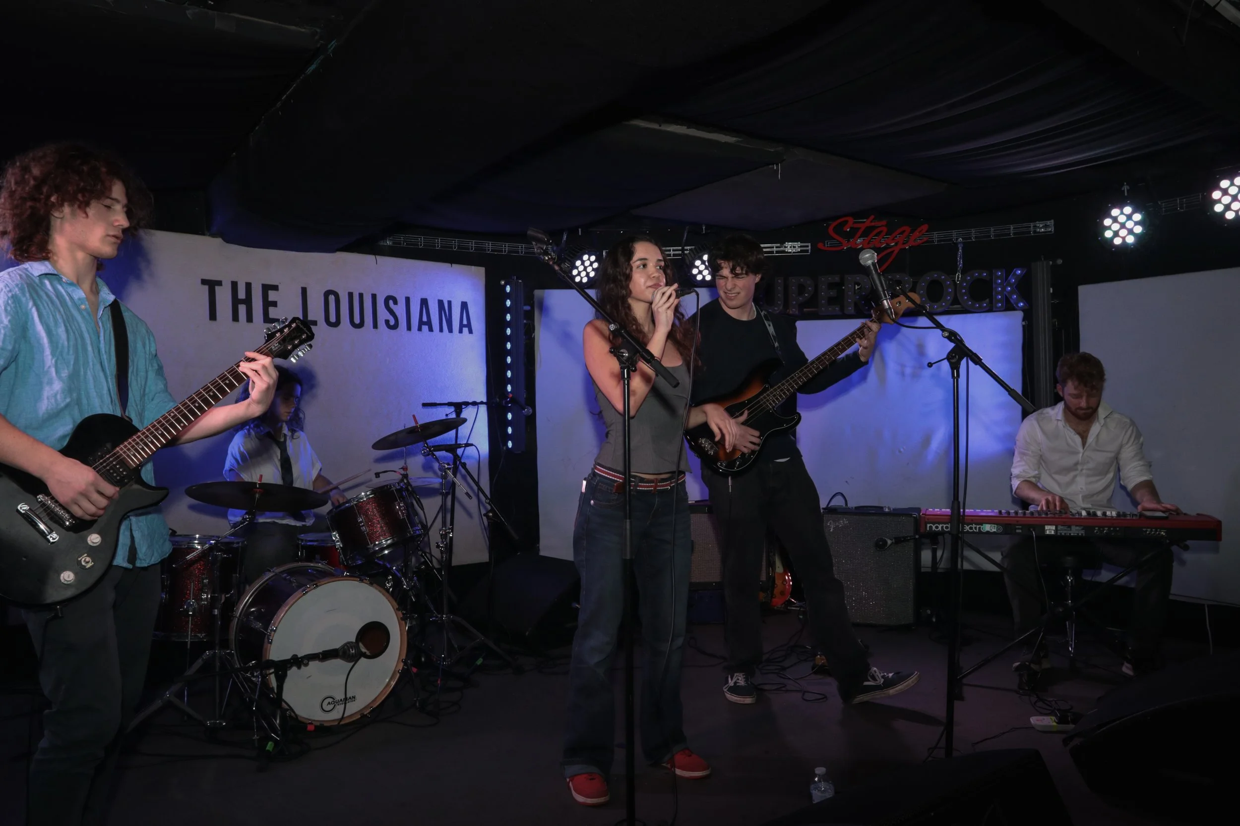 A band performing live on stage at a music venue with a sign that reads 'The Louisiana' in the background.
