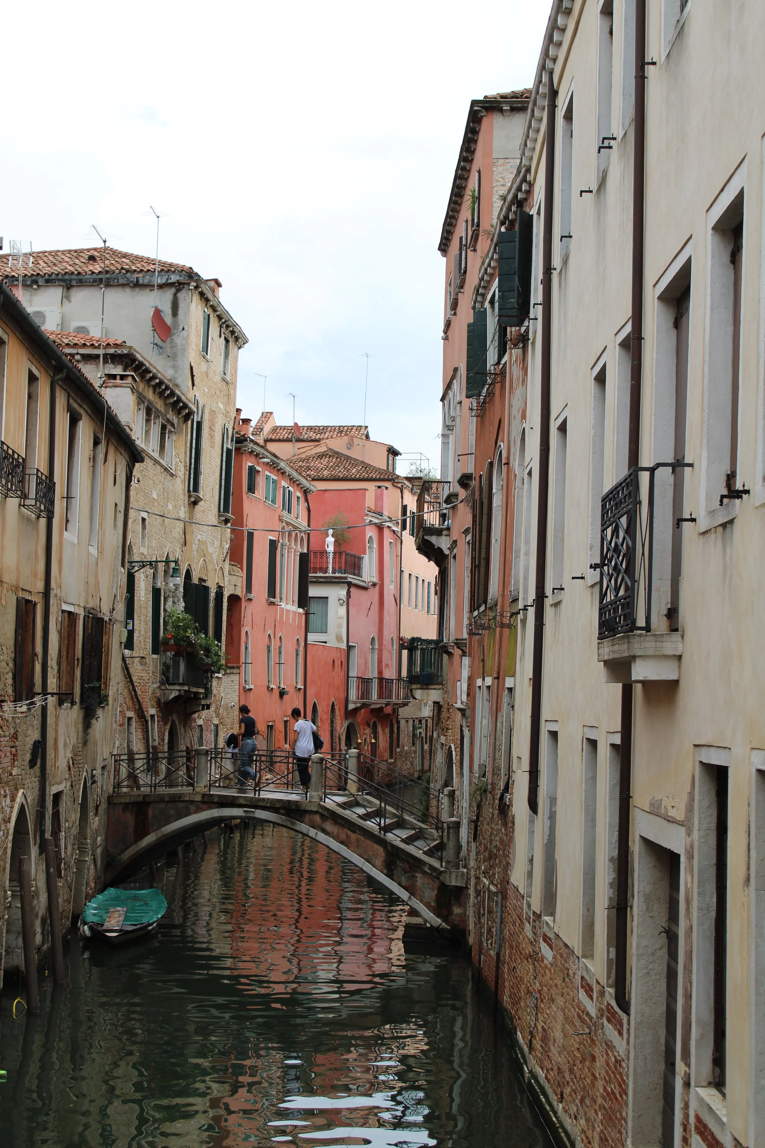 Colorful buildings lining a small canal with a bridge in Venice, Italy, and several people crossing the bridge.