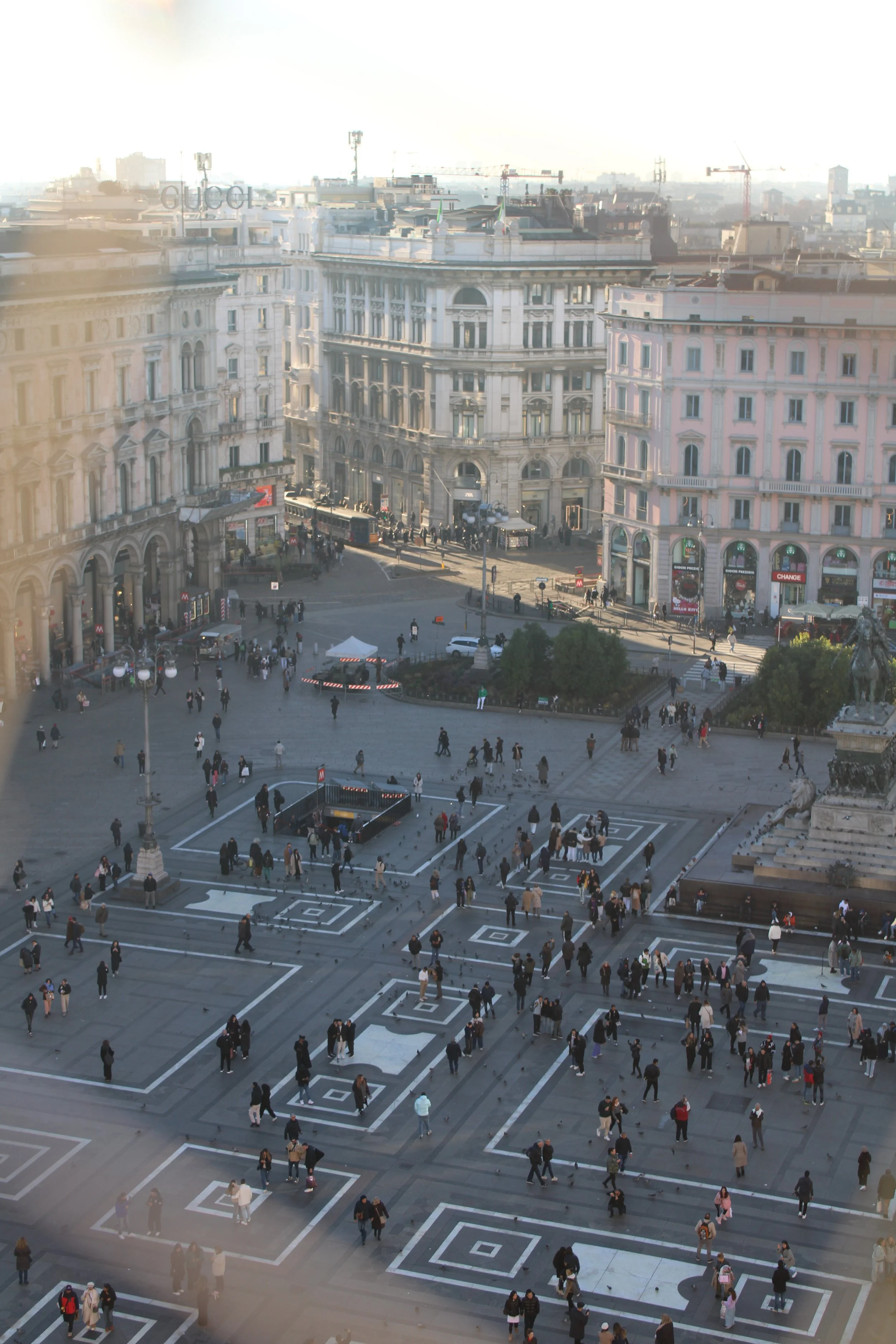 View of Piazza del Duomo in Milan, Italy, with people walking and historic buildings surrounding the square.