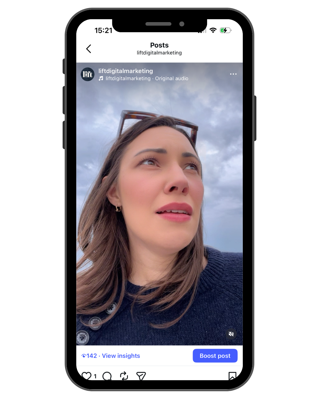 A woman with brown hair and sunglasses on her head looking up against a cloudy sky, taking a selfie on a smartphone.