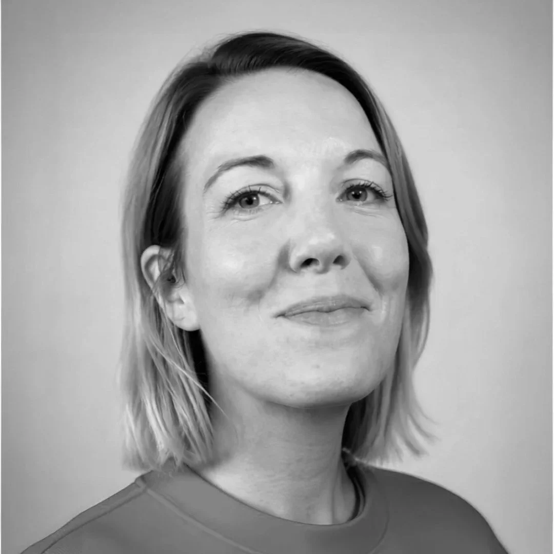Nichol looking slightly to the side and smiling subtly wearing a casual shirt in a black-and-white portrait.