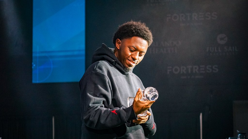 A young man in a black hoodie smiling while holding a crystal trophy or award