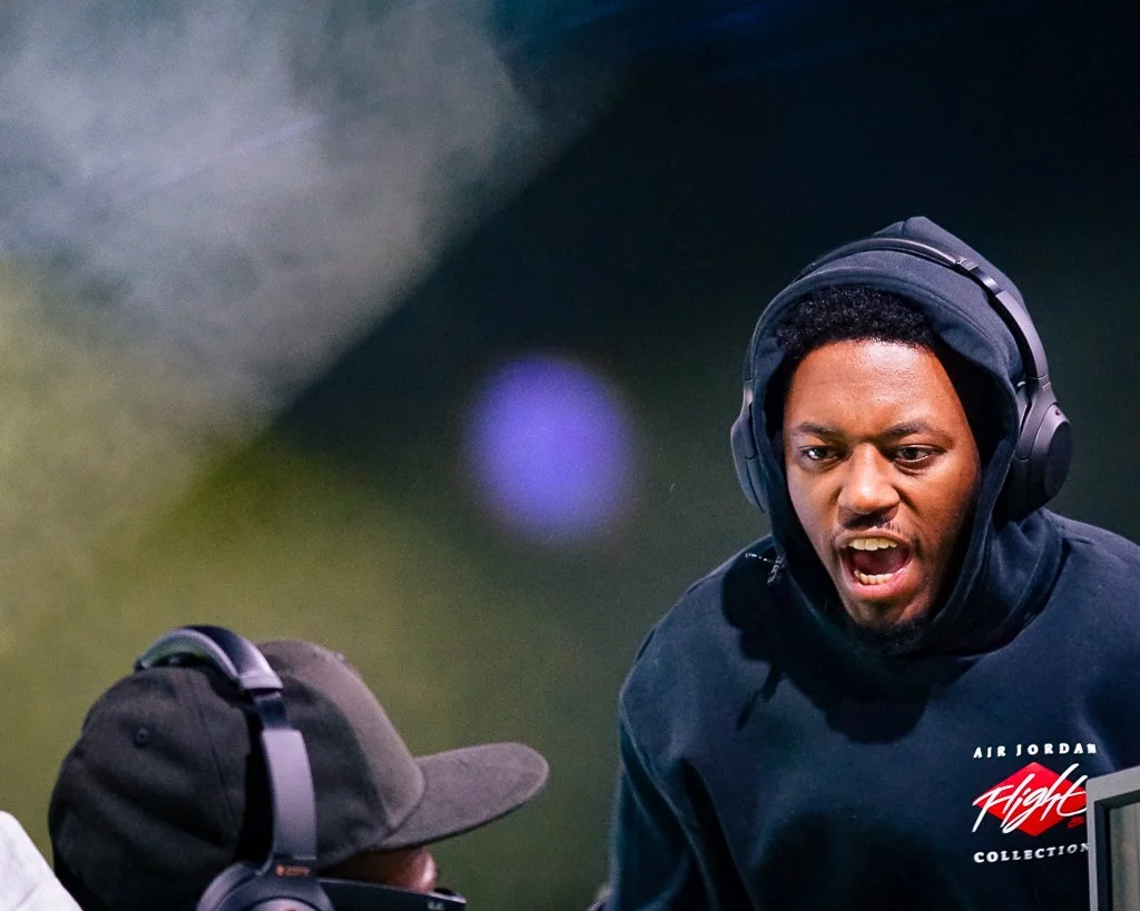 A young man with headphones shouting at a person in a hoodie and cap, both wearing headphones, during a football game.