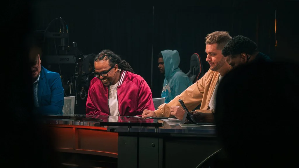 People sitting around a table, some smiling and laughing, in a studio or conference setting.