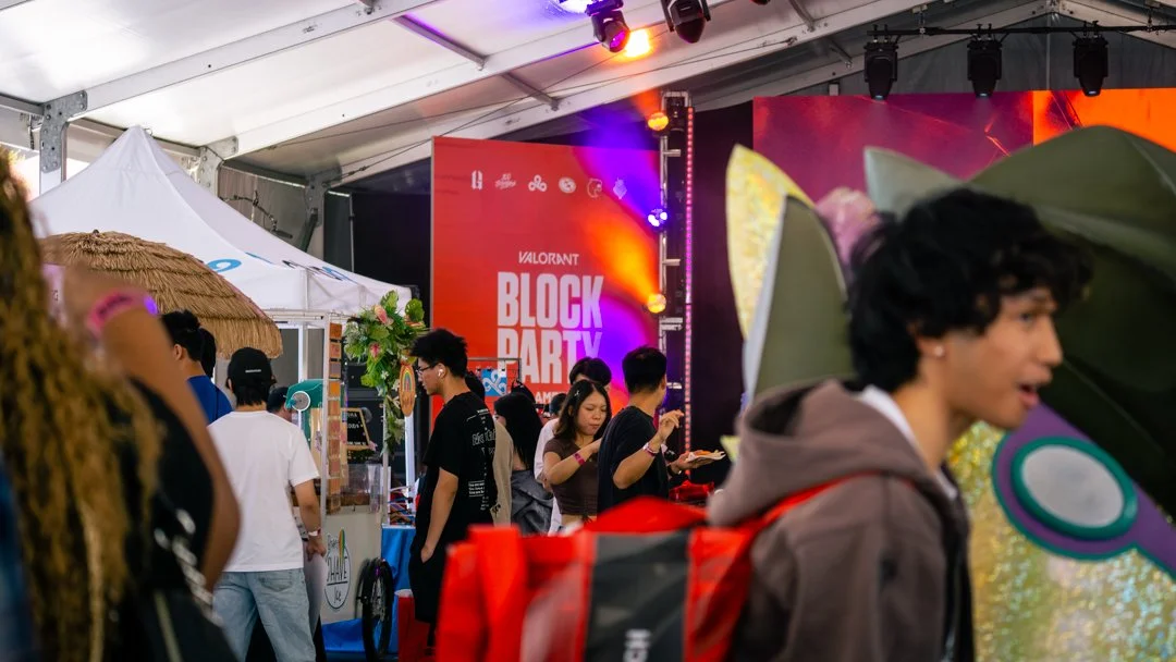People attending a Valorant Block Party event in LA inside a large tent with booths and colorful lighting.