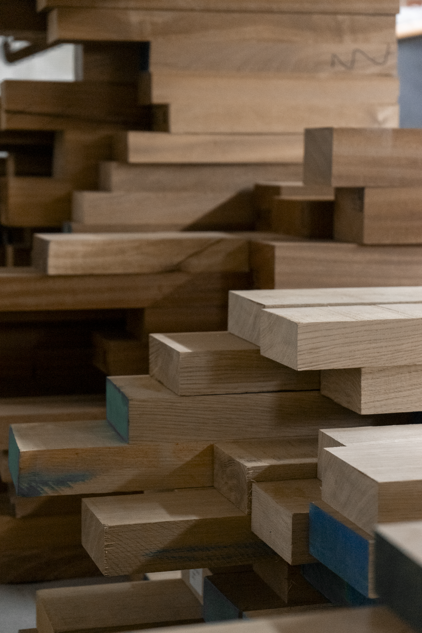 Stacked wooden planks in various sizes and shades, some with colored tips, arranged in a layered display.