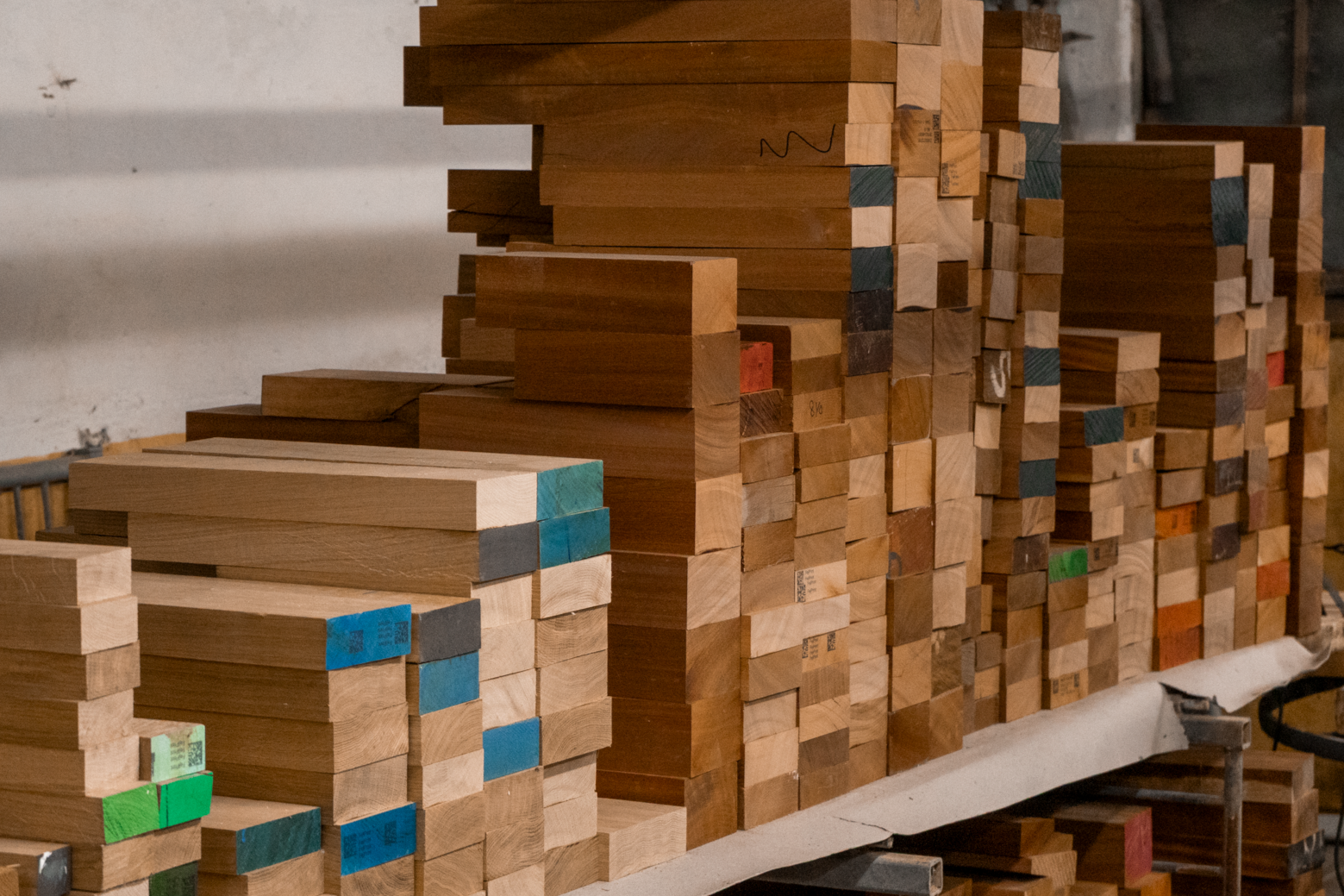 Stacks of wooden planks and blocks, organized on a workbench in a woodworking shop.