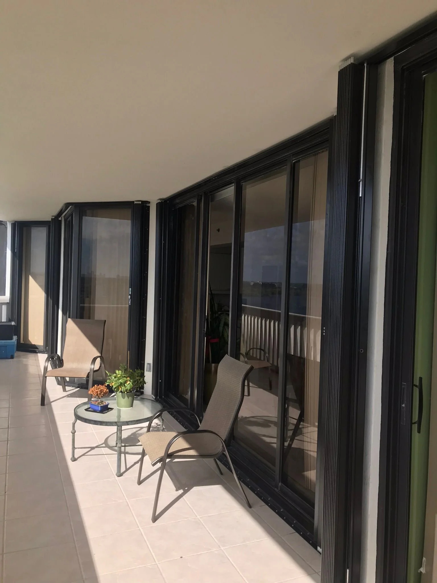 Balcony with beige chairs, a small round table with potted plants, and large sliding glass doors leading inside.