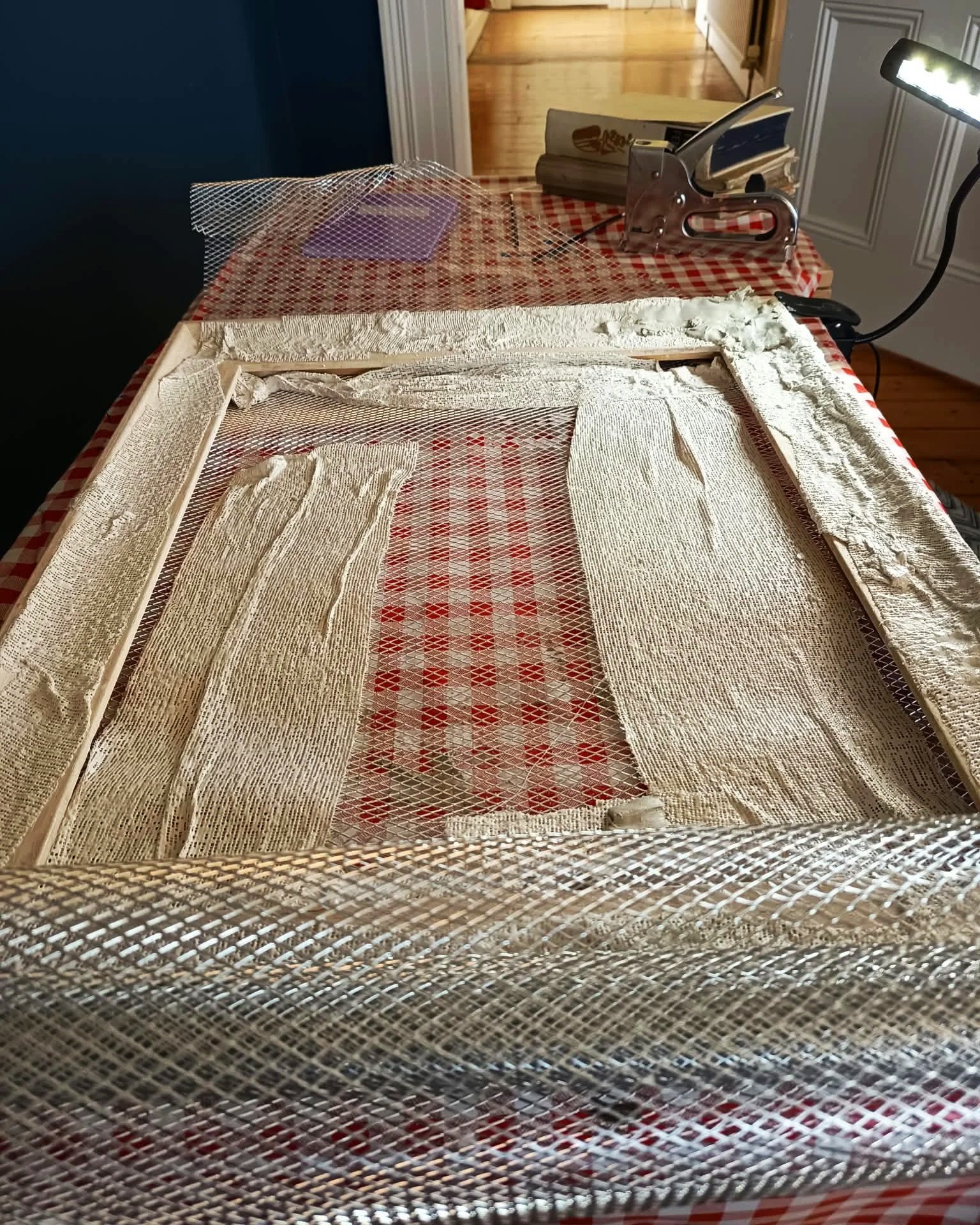 A stretched frame combining checked fabric and wire mesh, one of the found-material works in progress.