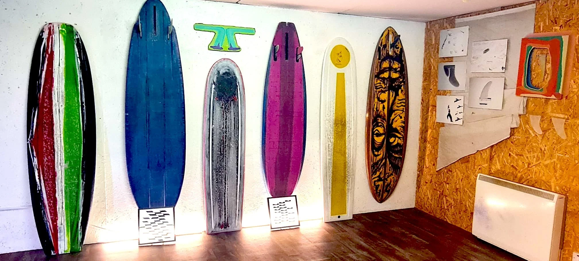 Six painted surfboards shaped by Elvis Beetham, in bold colour and pattern, displayed on the wall as part of WAKE III at Buoys & Gulls, Bundoran.