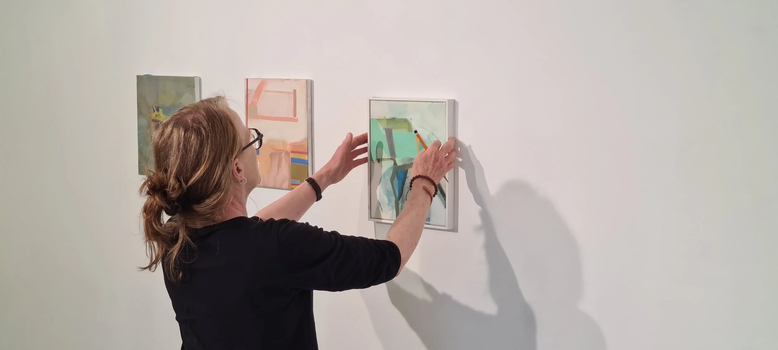 Patricia Doherty adjusting a painting on the gallery wall during installation of Unfixed Ground, Scenius Gallery Sligo