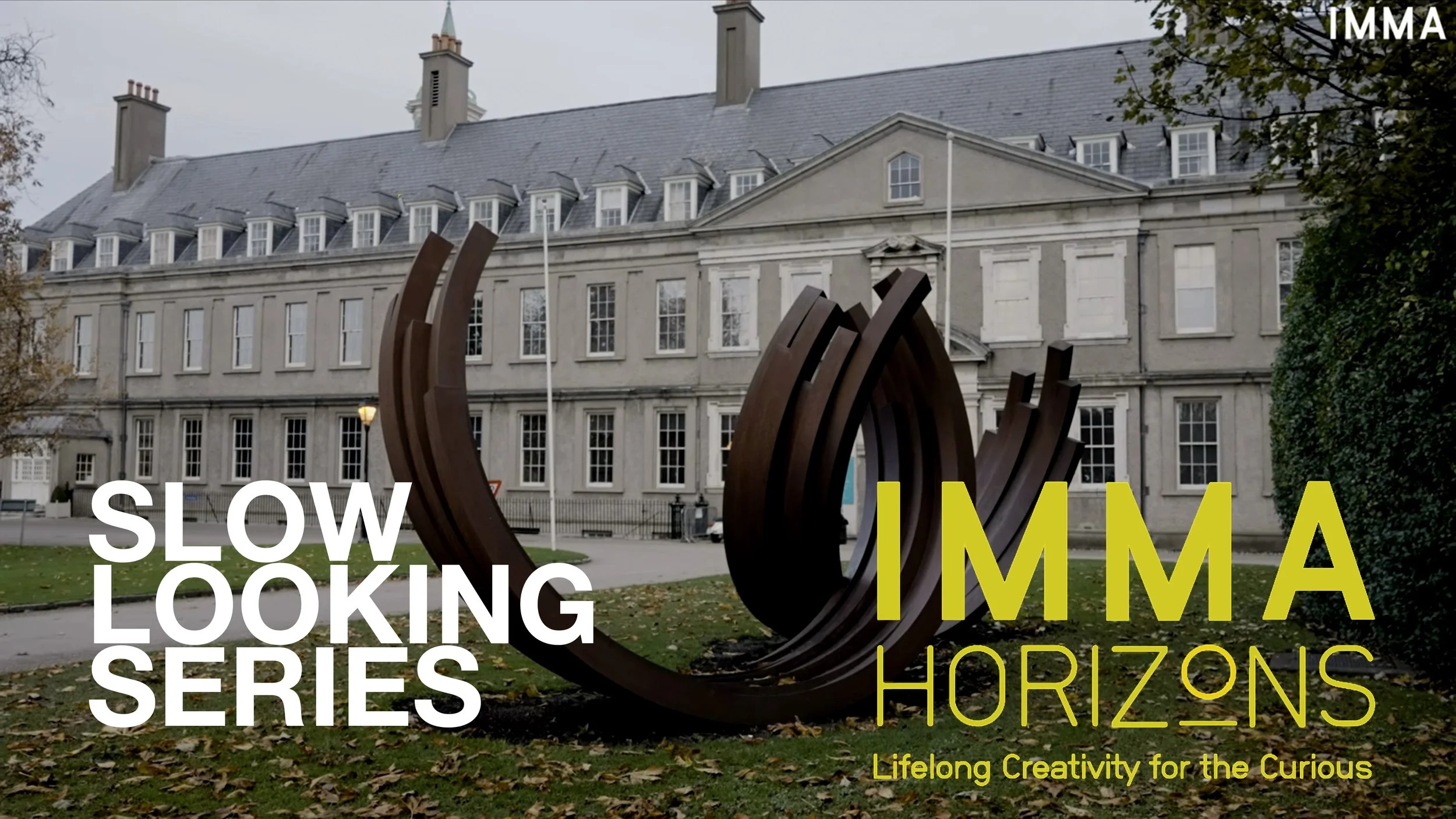 Public park with a modern curved sculpture made of metal in front of a large historical building with multiple windows and a slate roof.