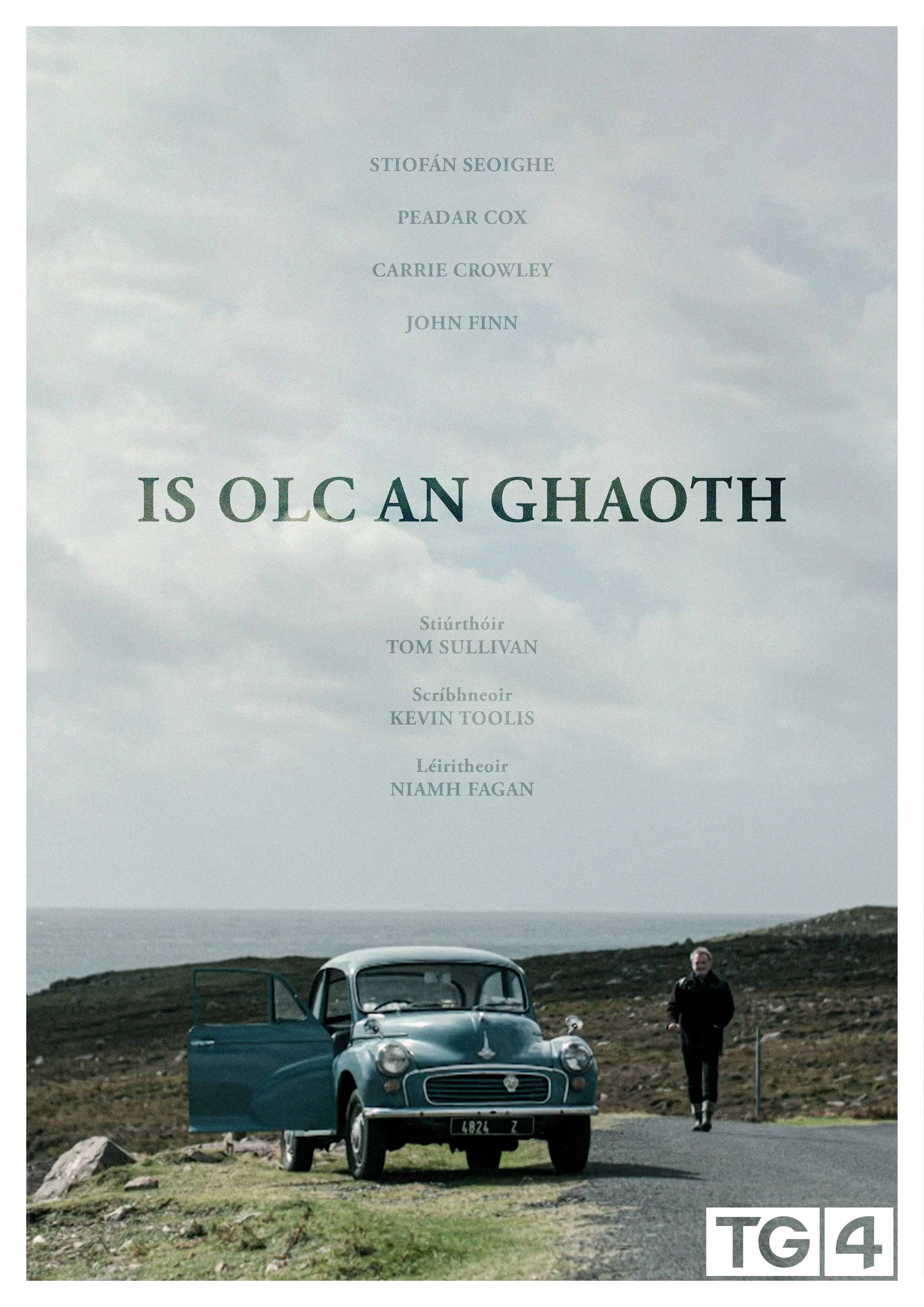 A cover page for a publication titled 'Is OLC An Ghaoth' featuring a vintage blue car parked on a rural road with an open door and a man standing nearby, with cloudy skies and open landscape in the background. 