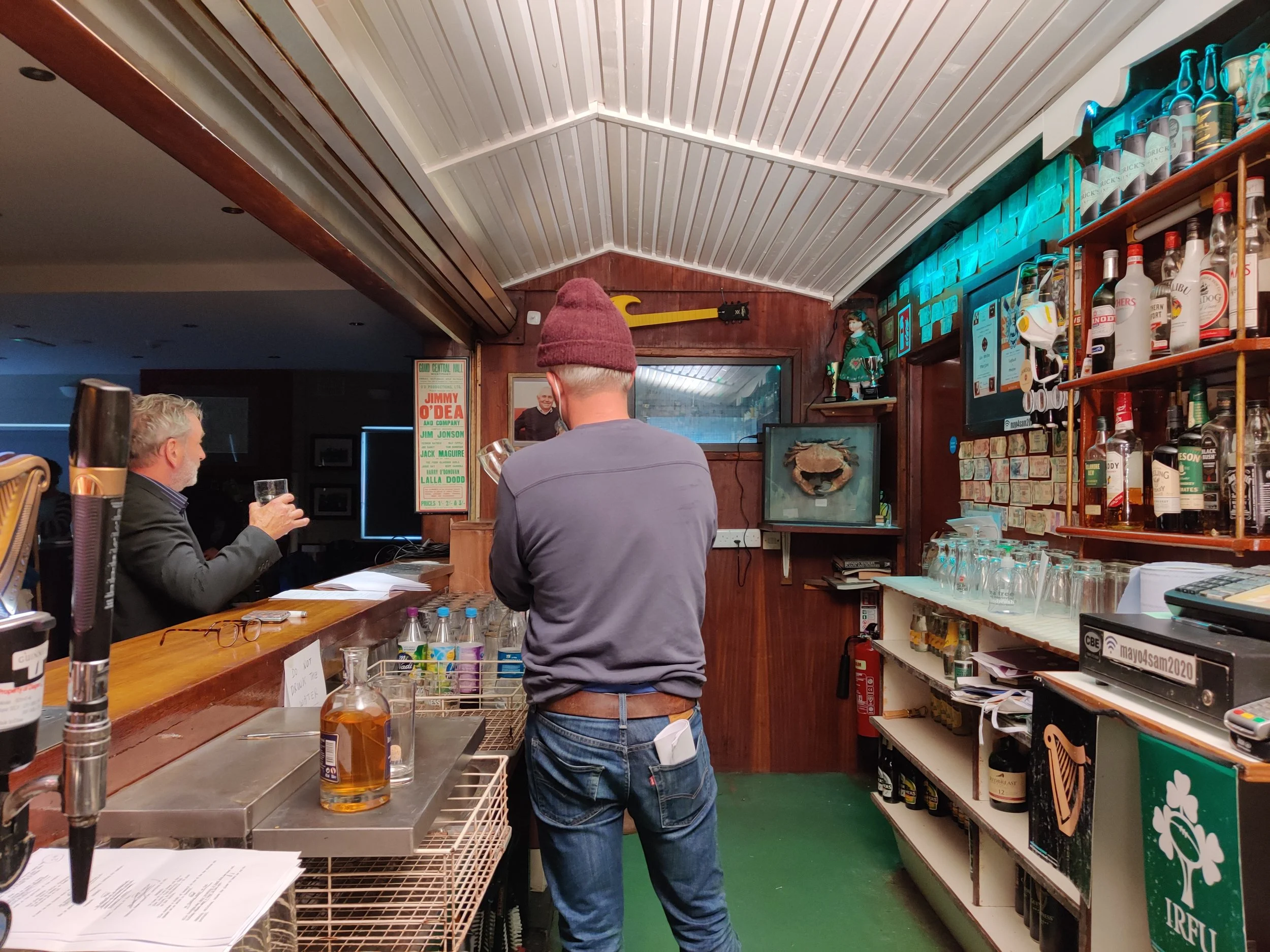 Behind the scenes photo. People inside a bar or pub with shelves of alcohol, a bar counter, and decor including a mounted crab on a wooden wall.