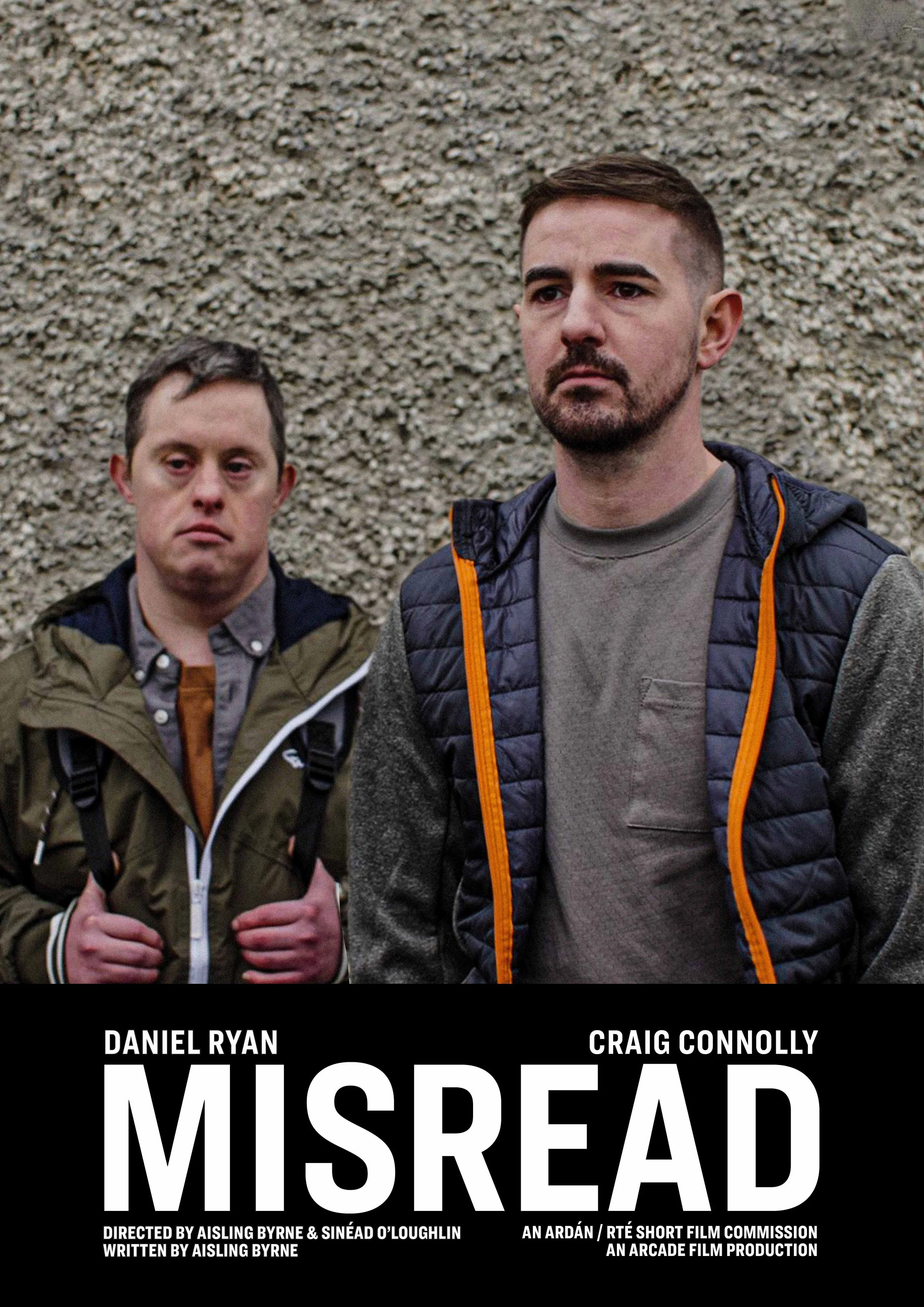 Poster for the film 'Misread' featuring two men standing in front of a rough-textured wall; one man in a gray shirt and black quilted vest, the other in a green jacket with a backpack.