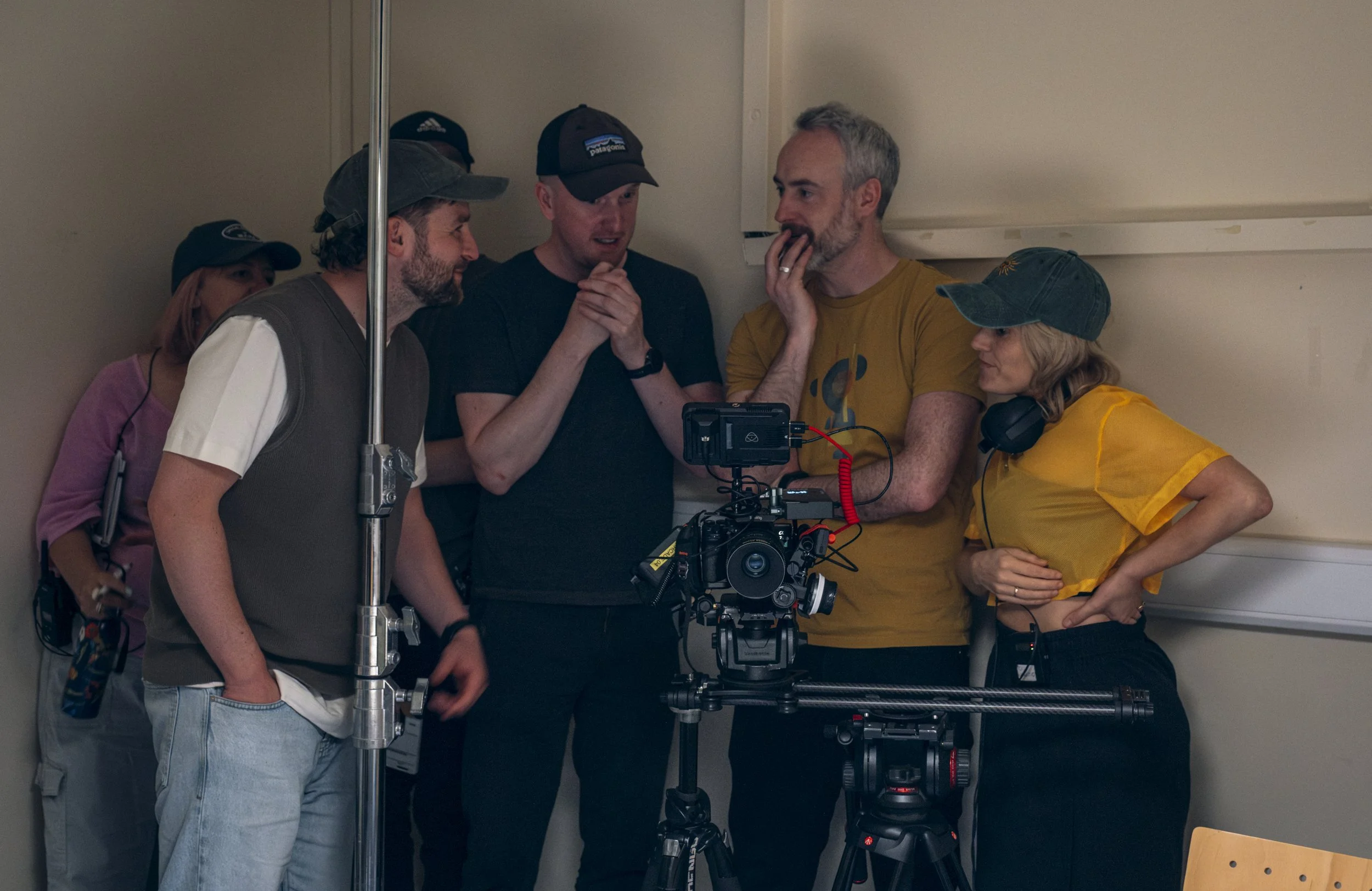 Group of six people gathered around a camera and filming equipment, discussing something while on a film set.