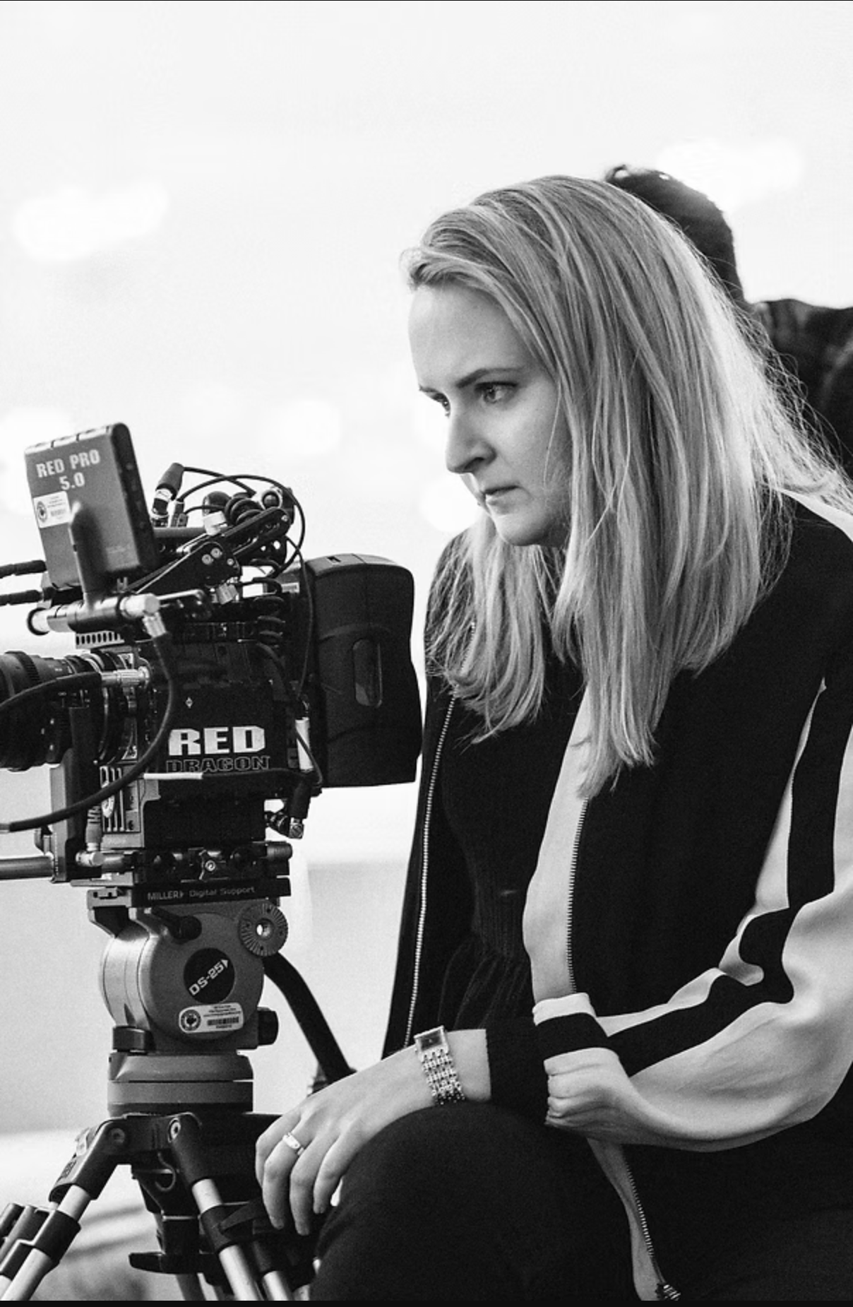 A woman with long hair operating a professional cinema camera on a tripod, focused on filming.