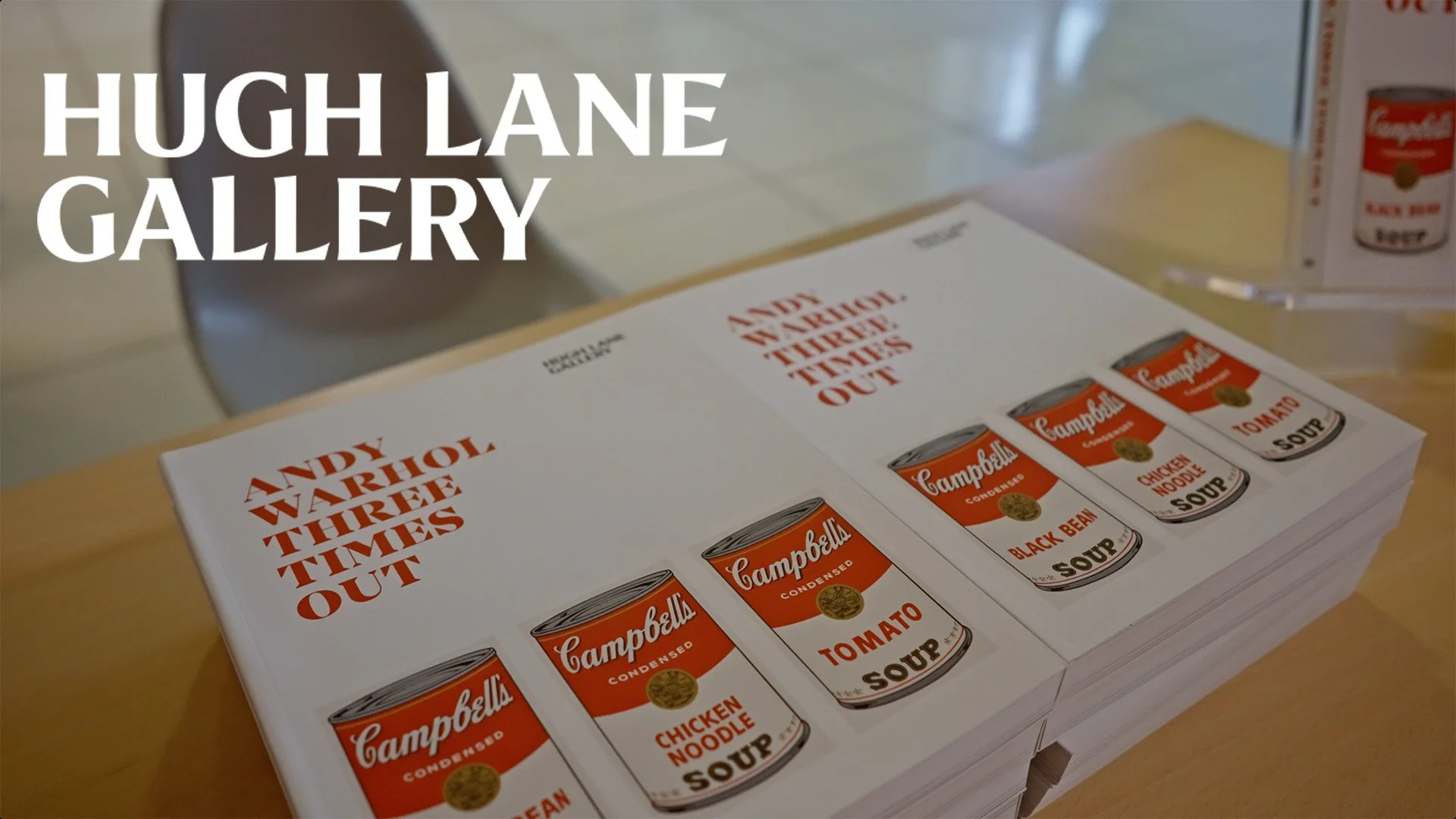A stack of books with covers featuring images of Campbell's soup cans and the text "Andy Warhol. Three Times Out." on a table.